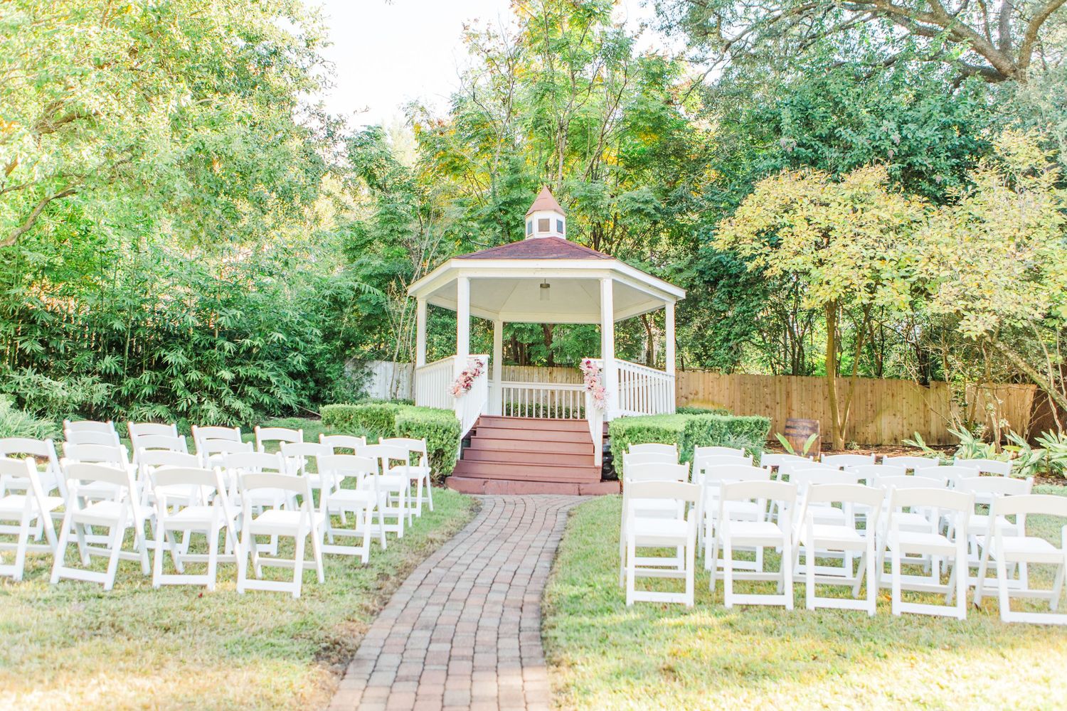 Outdoor wedding venue setup with white chairs and brick pathway leading to gazebo.