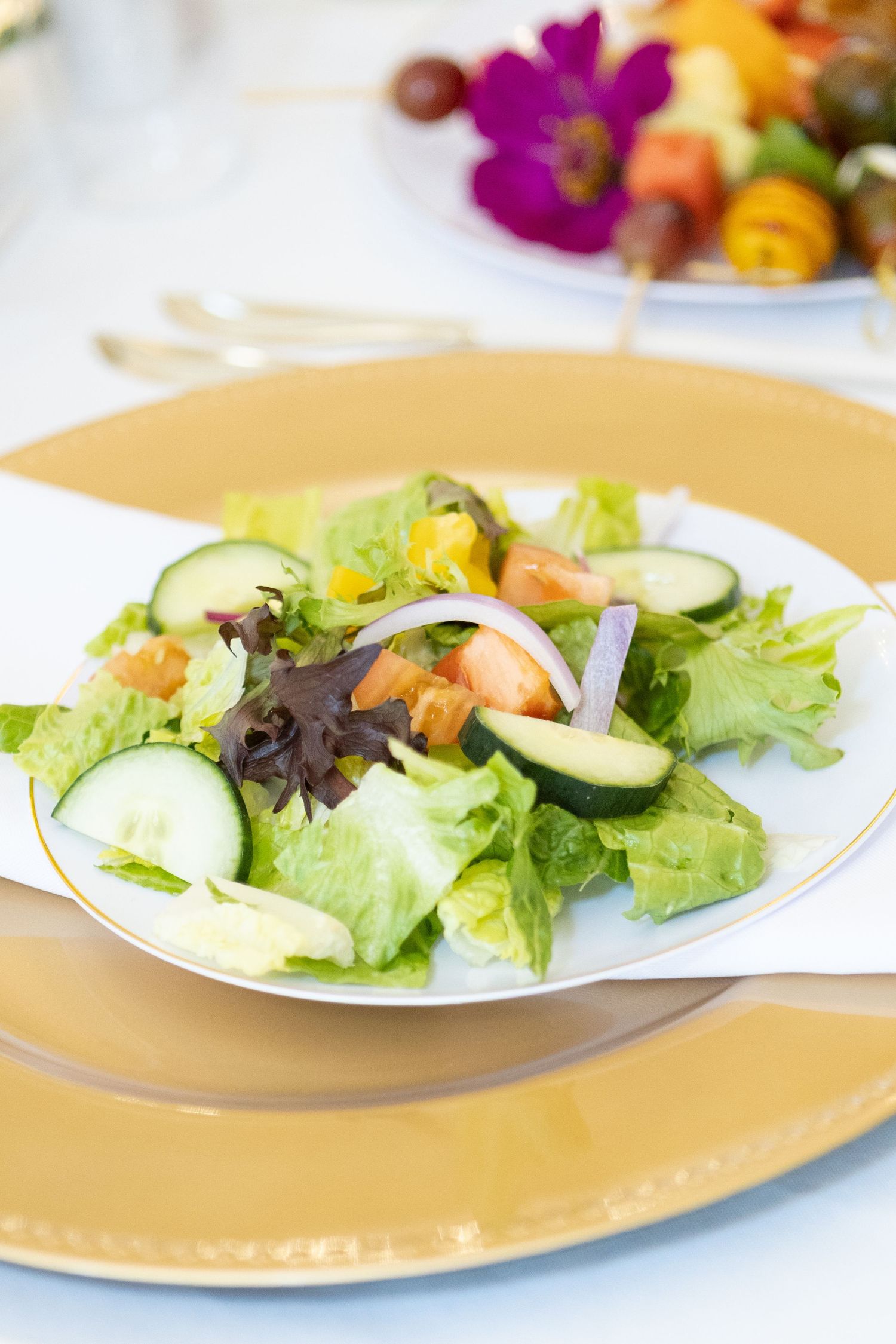 Fresh garden salad with lettuce, cucumber slices and mixed greens served on gold-rimmed plates.