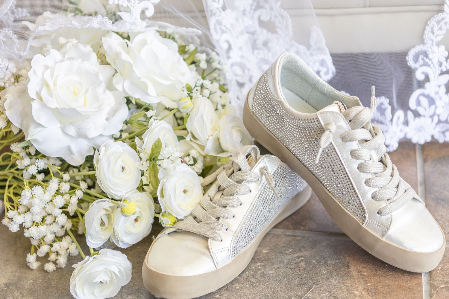 White bridal sneakers next to elegant white roses and baby's breath bouquet.