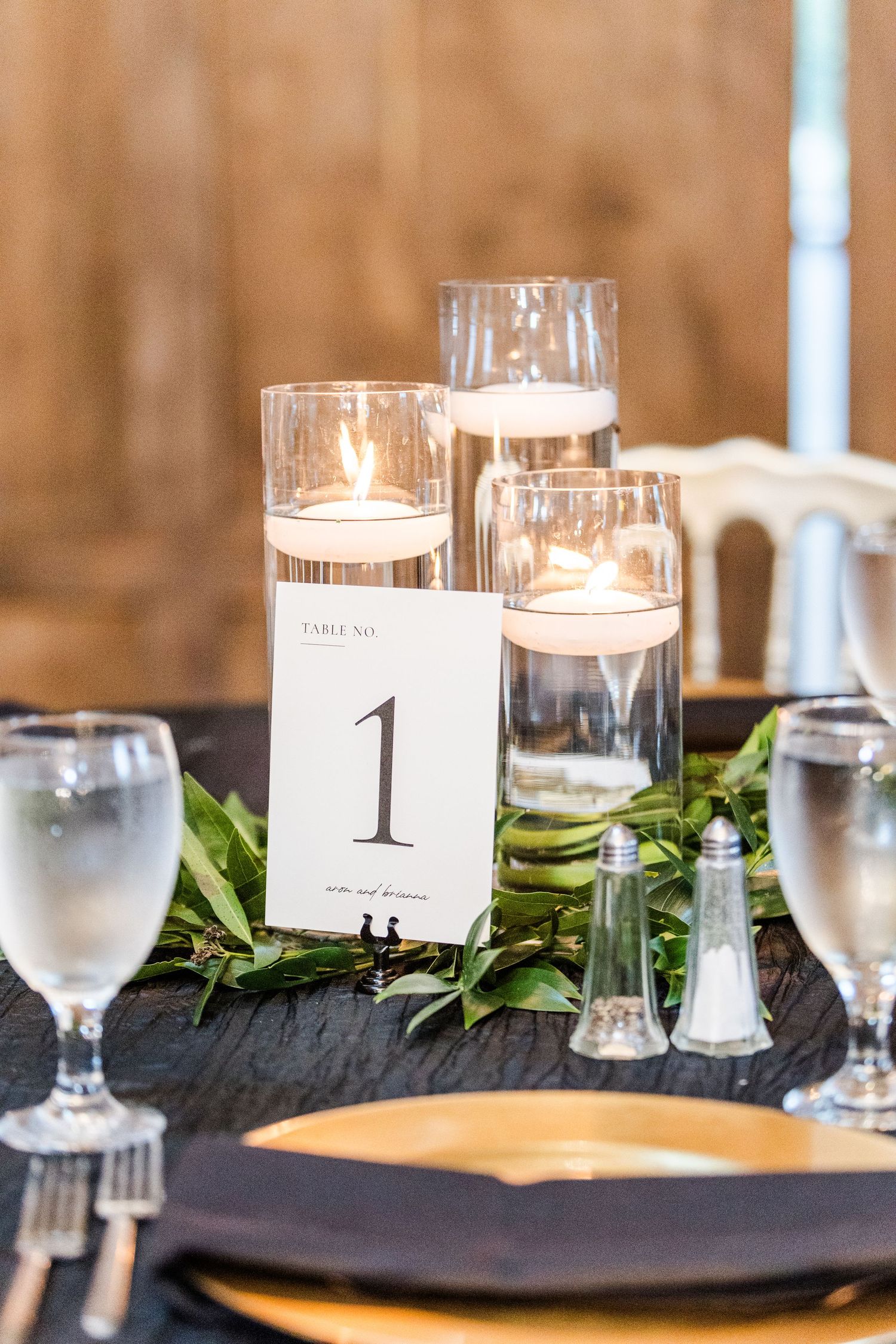 Elegant wedding reception table setting with candles, table numbers and greenery accents.