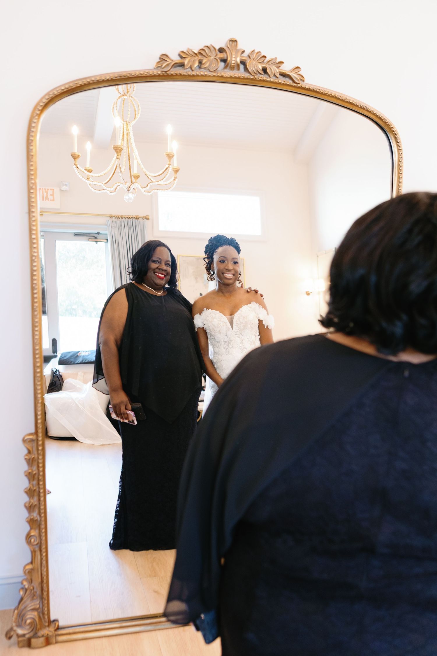 People wearing black attire gathering in a room with ornate gold-framed mirrors.