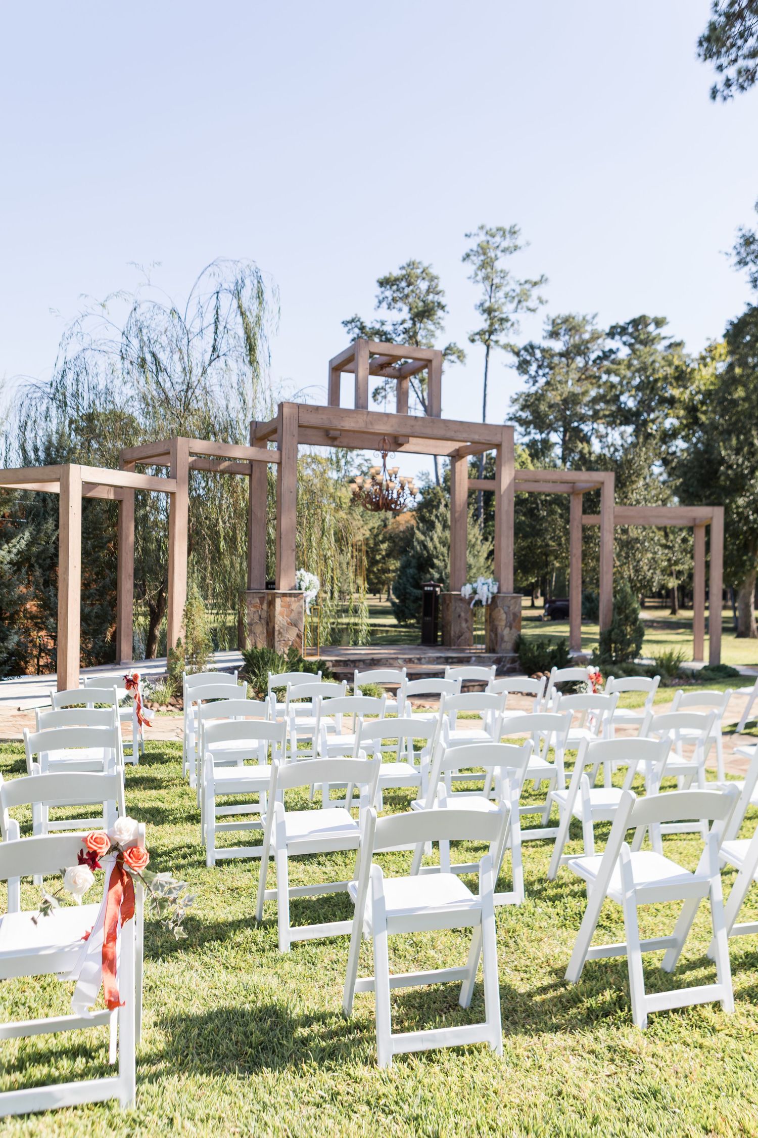 White wooden chairs arranged in rows for an outdoor wedding ceremony with wooden pergola structures in the background.
