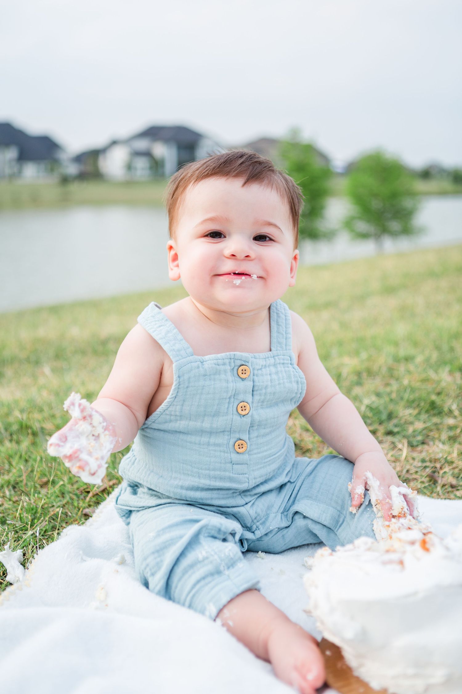 Outdoor cake smash photo session featuring light blue overalls on grass.