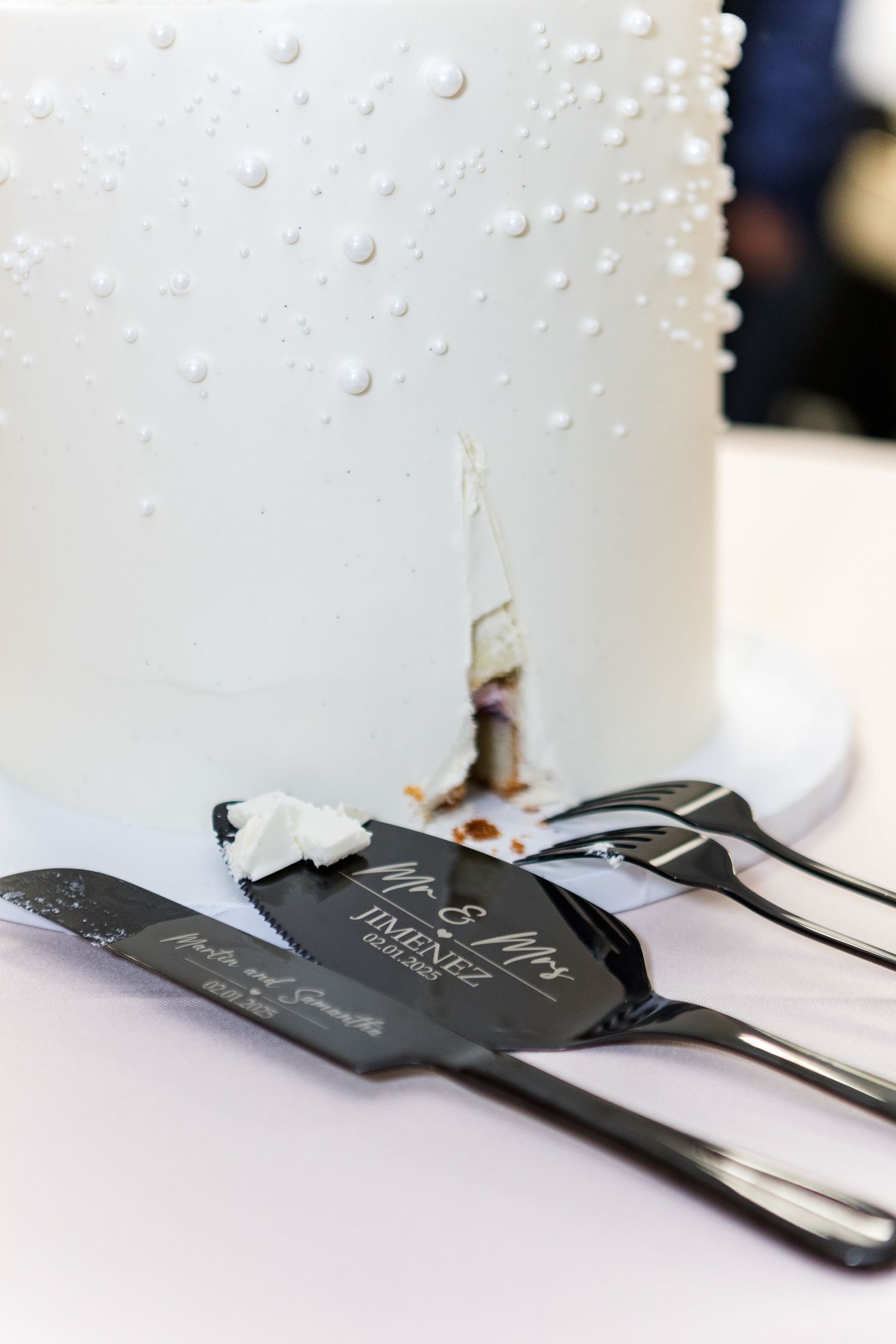 Close-up of pearl details on a white wedding cake with black place cards.