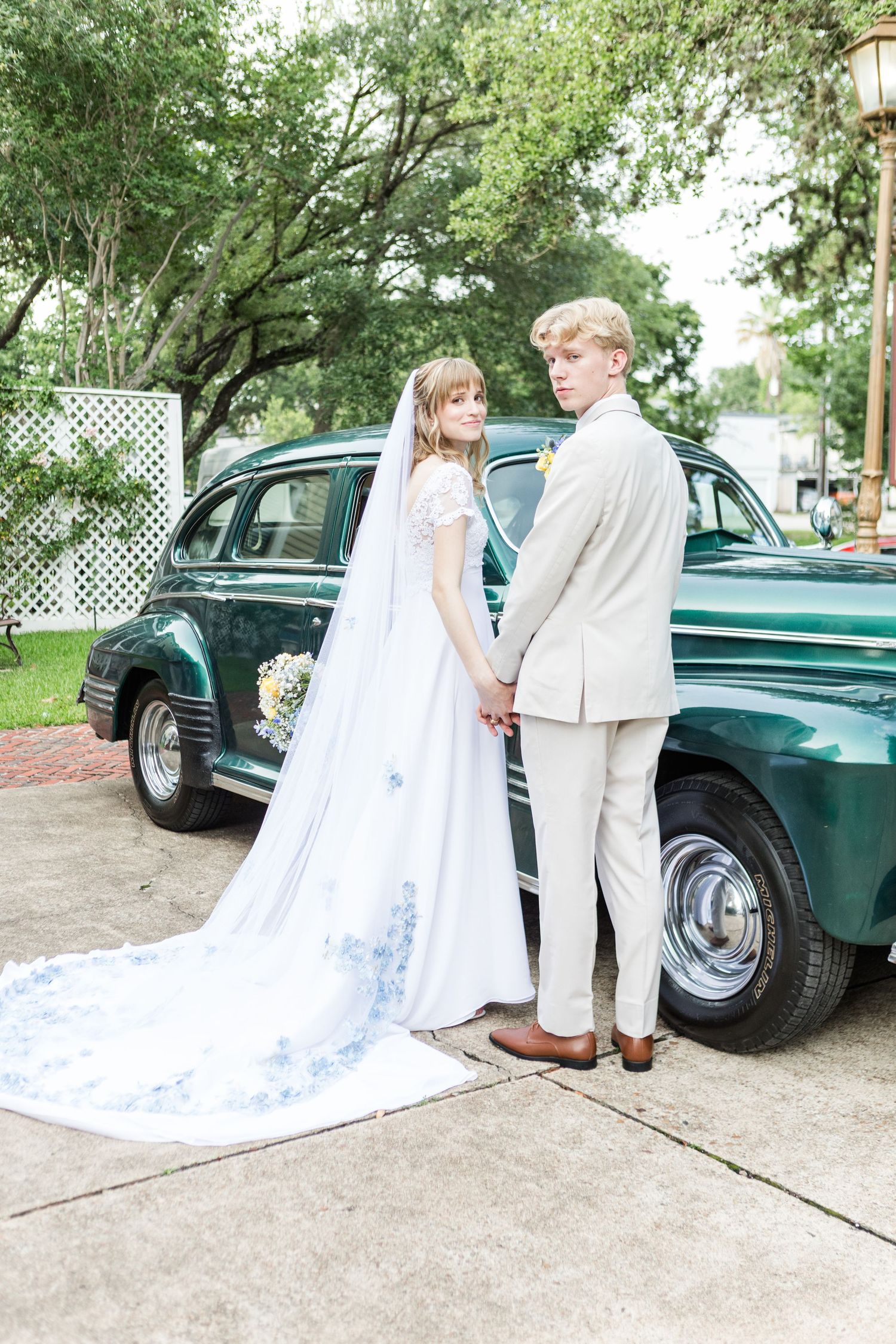 Wedding couple posing with classic green vintage car on garden path.