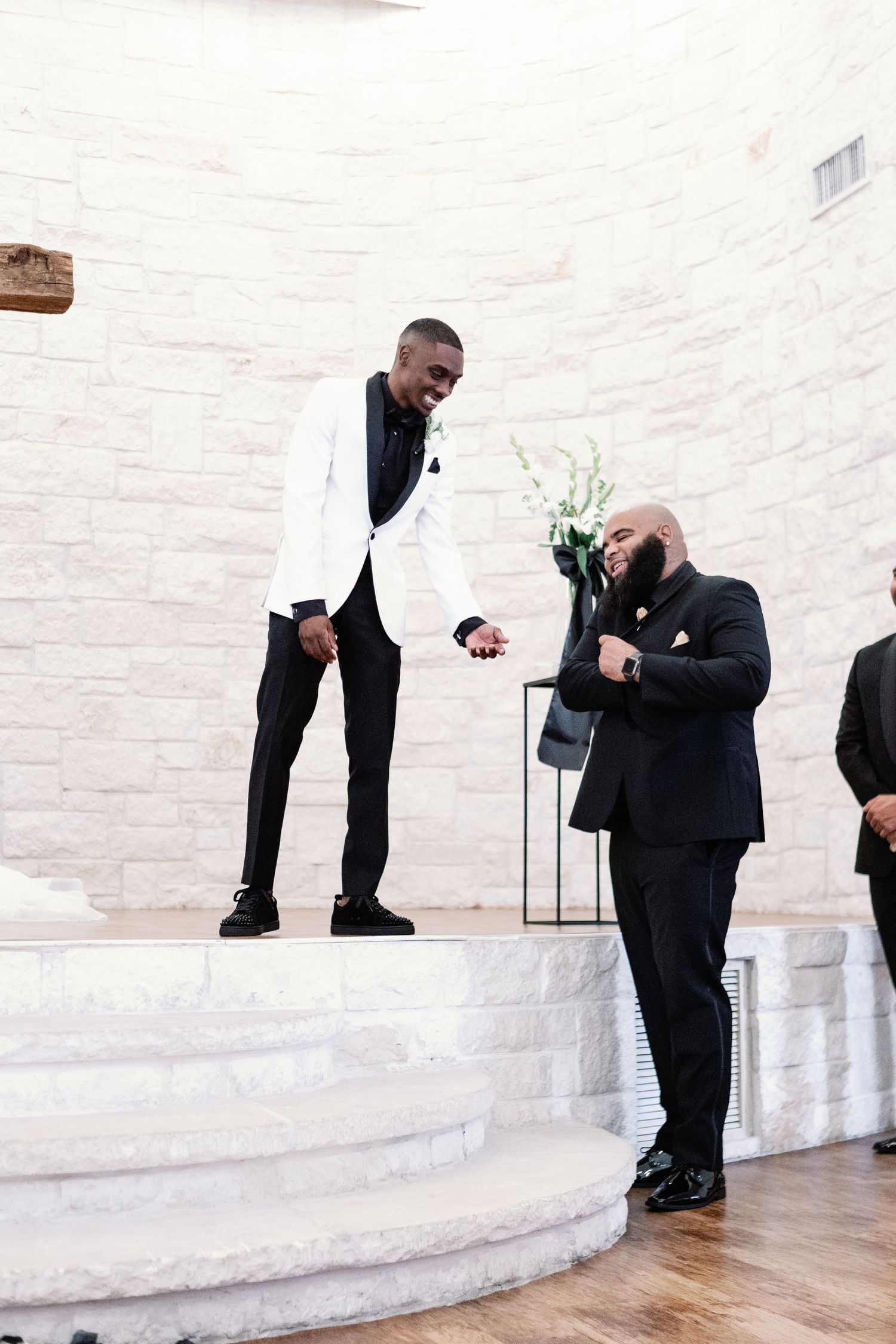 People in formal black attire engage in a ceremonial toast at an elegant white venue with hardwood floors.