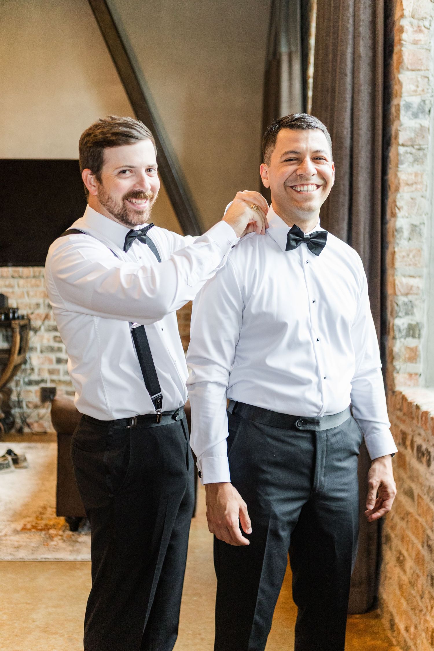 A joyful moment captured showing wedding party members in formal attire with white shirts and dark pants in an indoor setting.