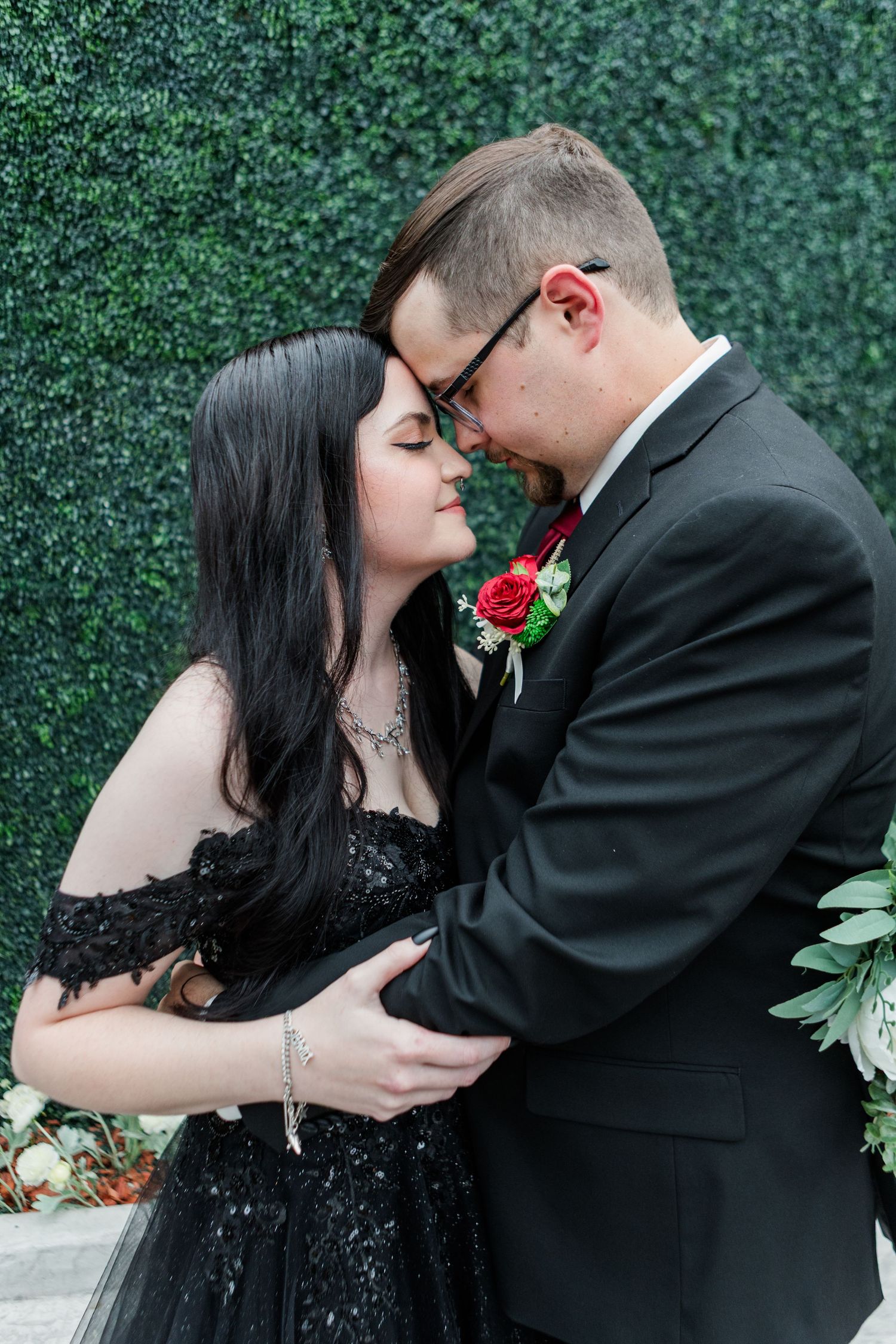Romantic embrace during wedding photoshoot against emerald hedge backdrop.
