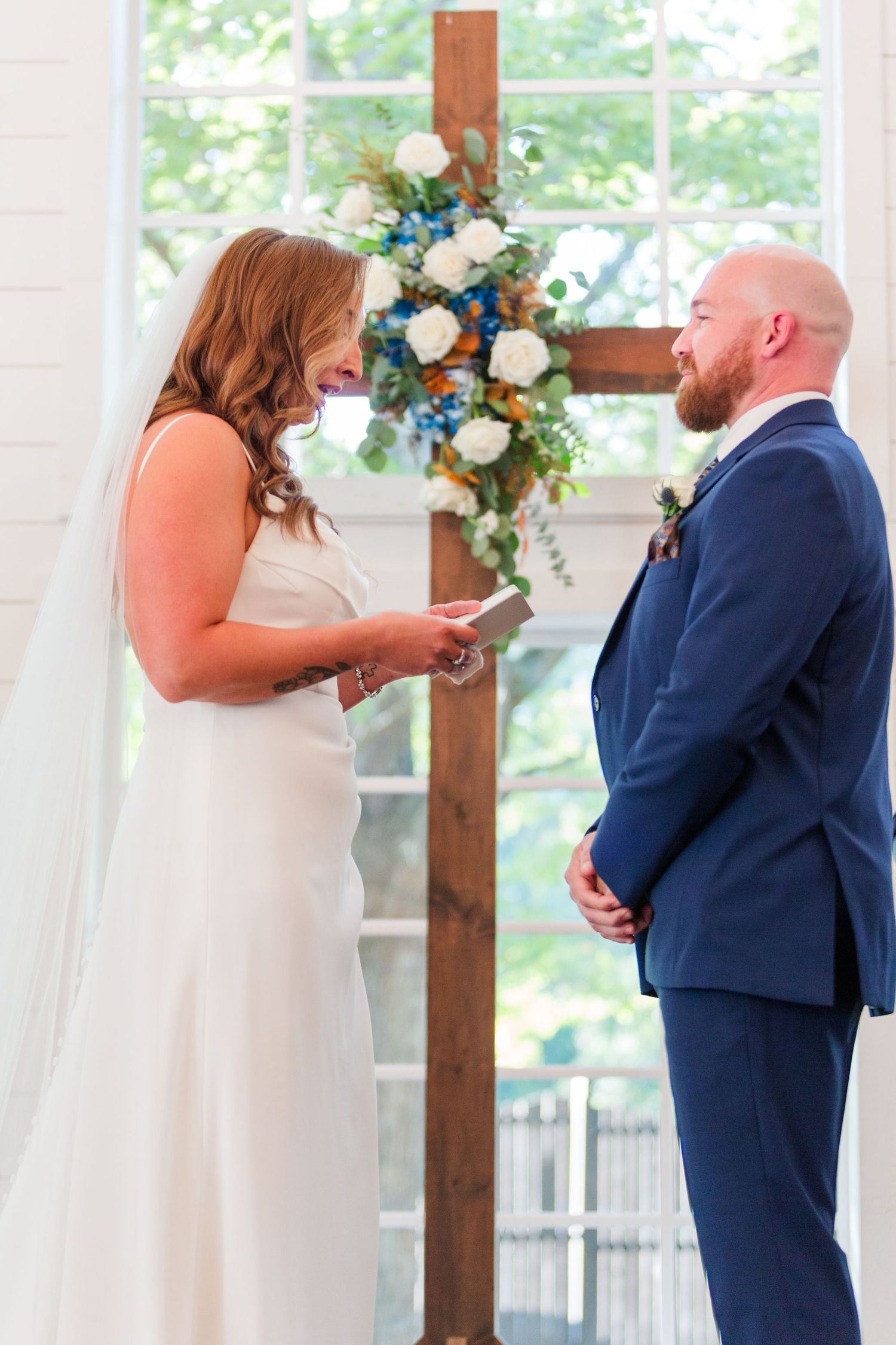 Bride and groom exchanging vows in front of floral cross decoration.