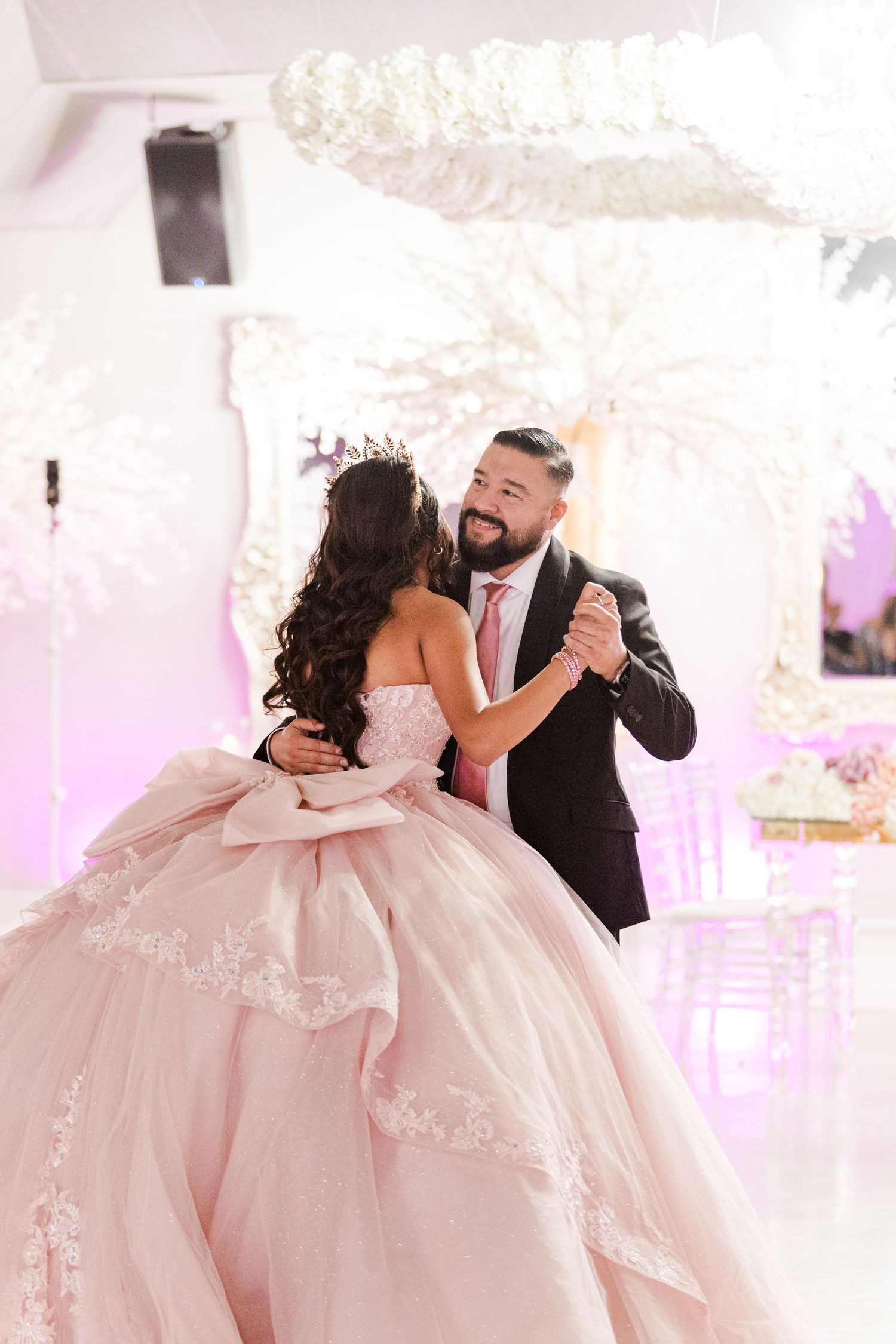Couple dancing in an elegant pink and white decorated venue with flowing pink ball gown.