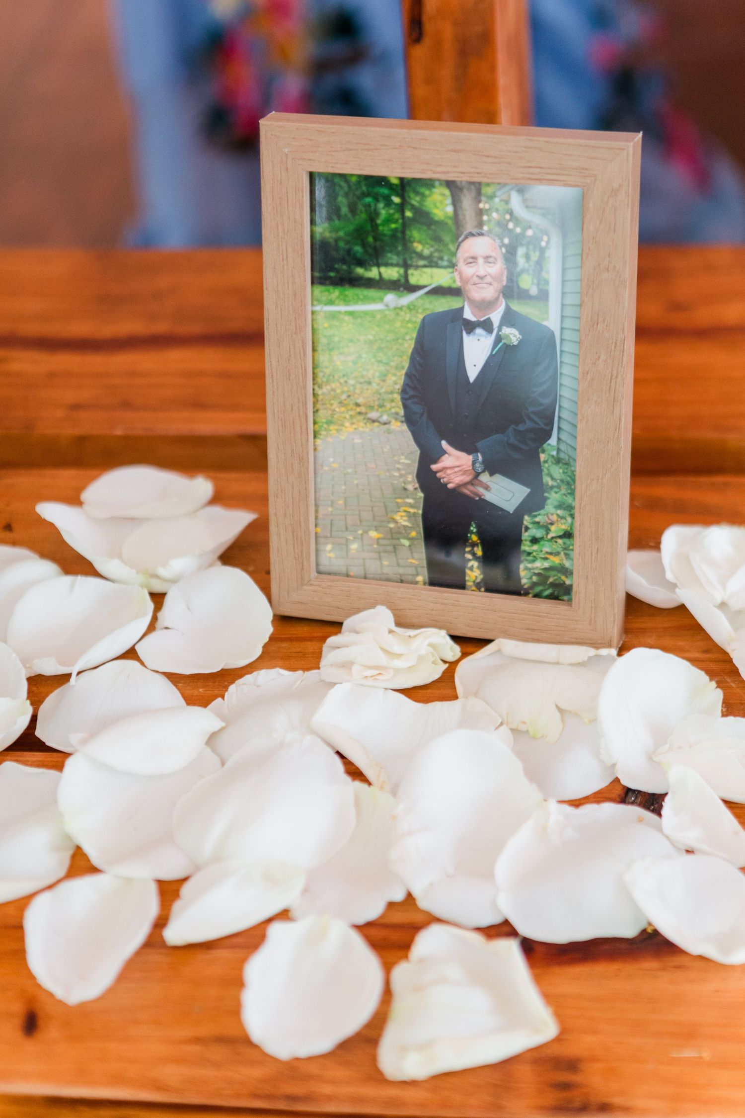 White rose petals scattered on a wooden surface with framed photographs.