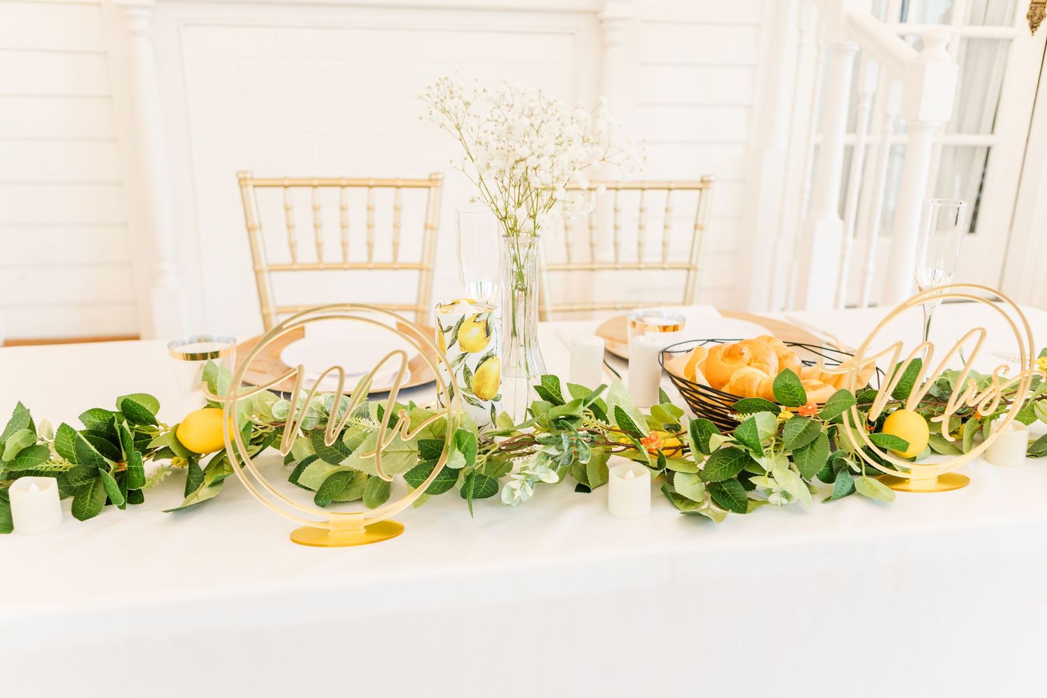 Elegant reception table setup with gold chiavari chairs and green garland decorations.