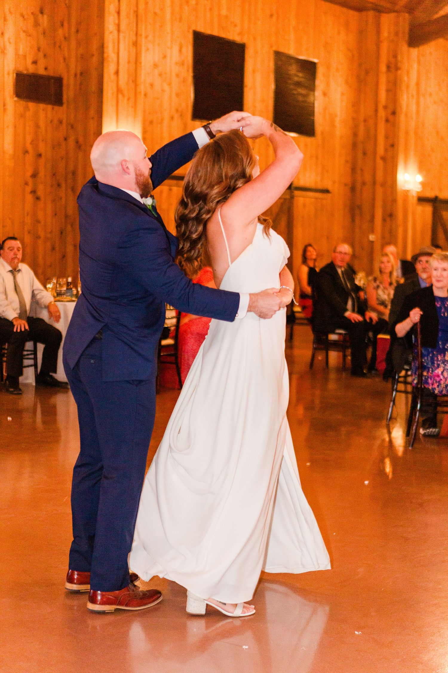 Wedding couple dances together in a warmly lit wooden reception hall.