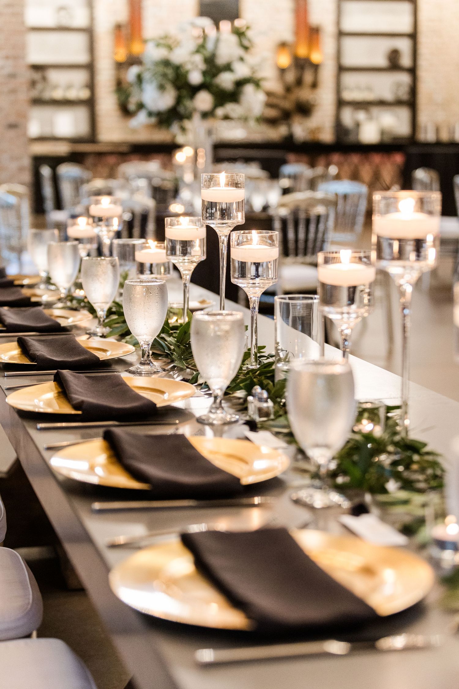 Elegant wedding reception table setting with black napkins, floating candles, and greenery garland decor.