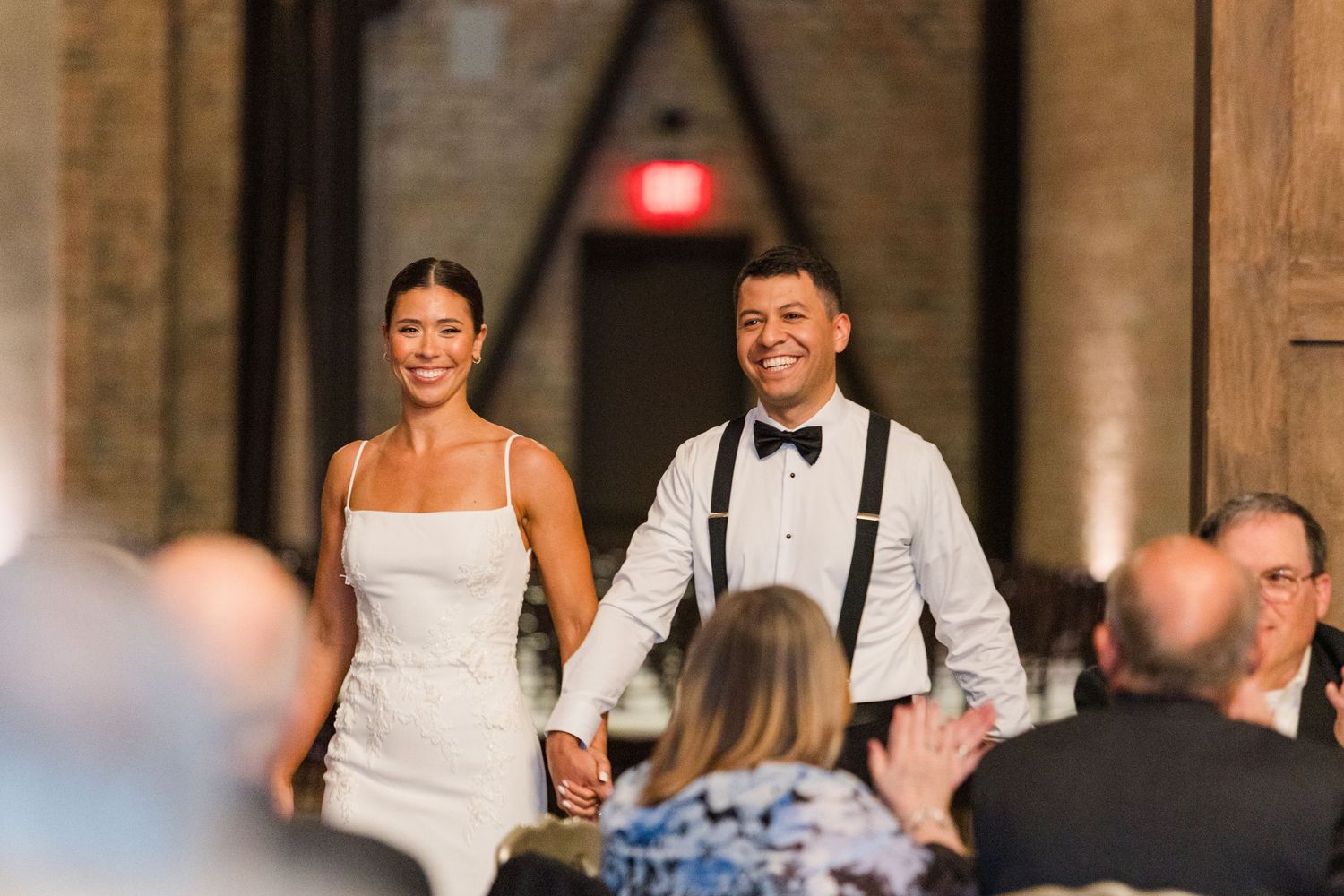 Wedding guests dancing and celebrating in an elegantly decorated reception hall with warm lighting.