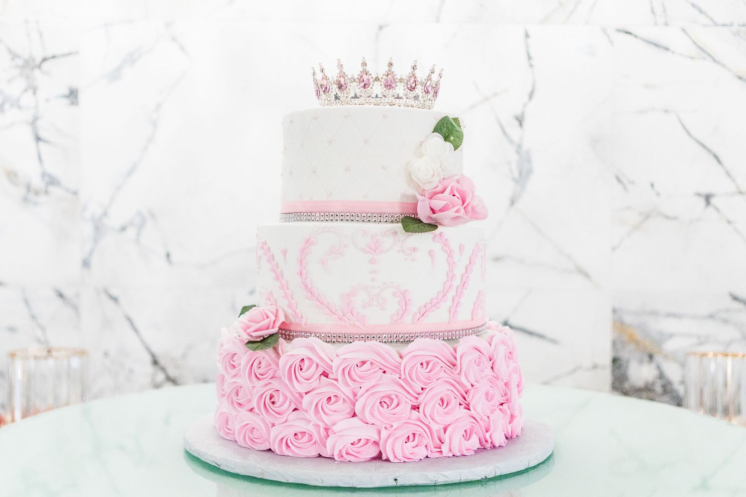Pink princess-themed cake decorated with roses and crown on white marble background.