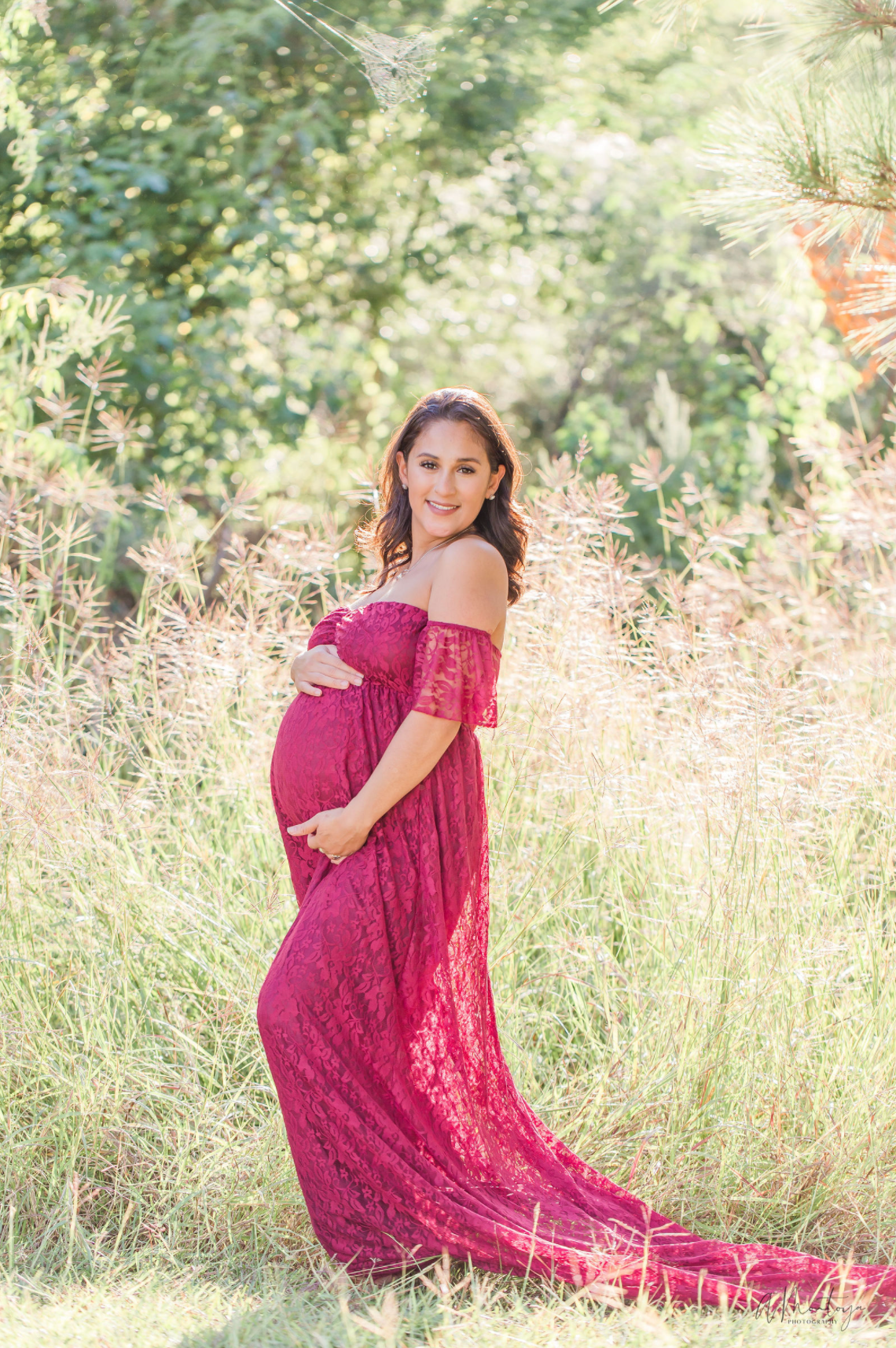 Woman in red lace dress poses elegantly in sunlit meadow during photo session.