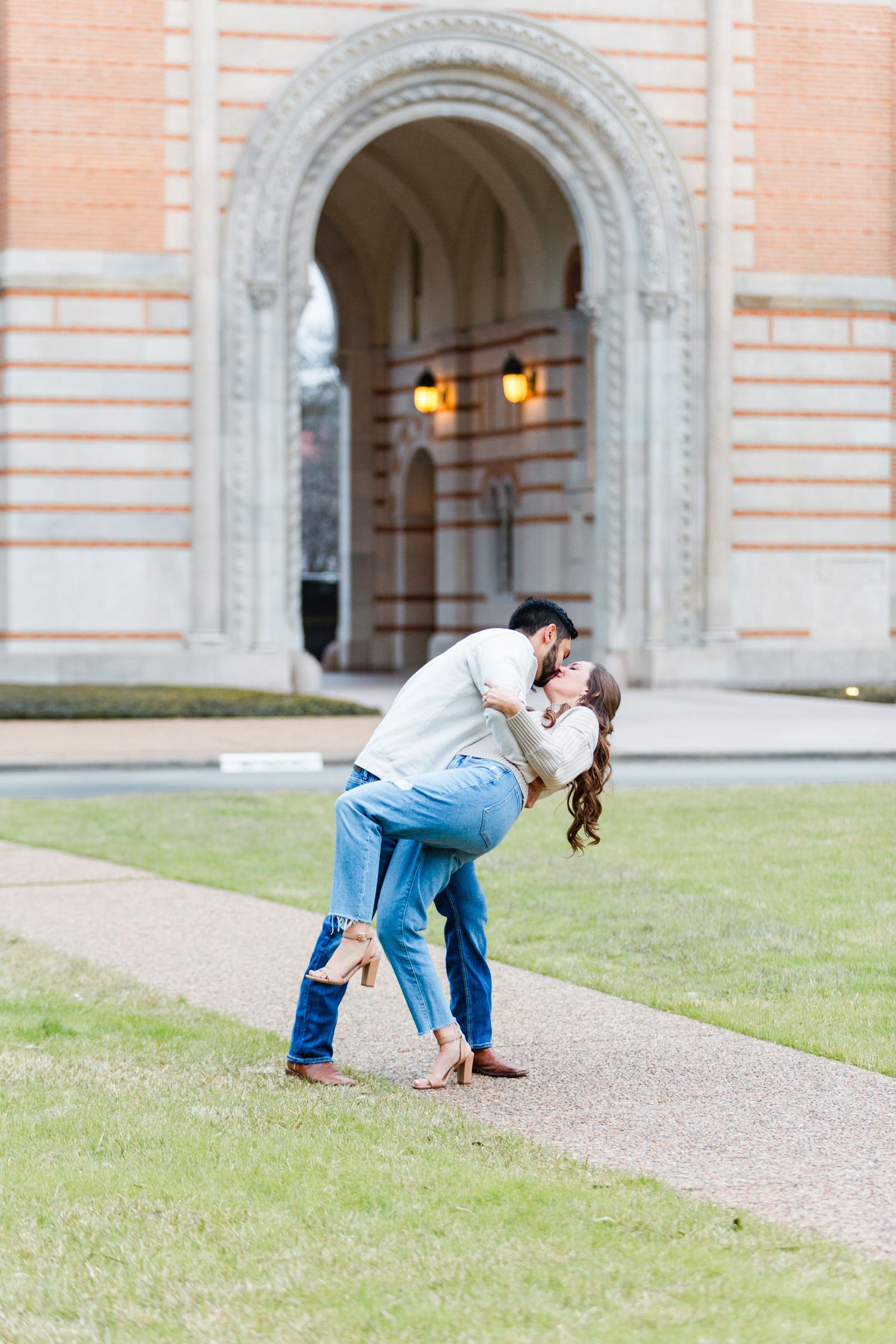 Couple engaged in playful dip kiss pose outside historic building with archways.