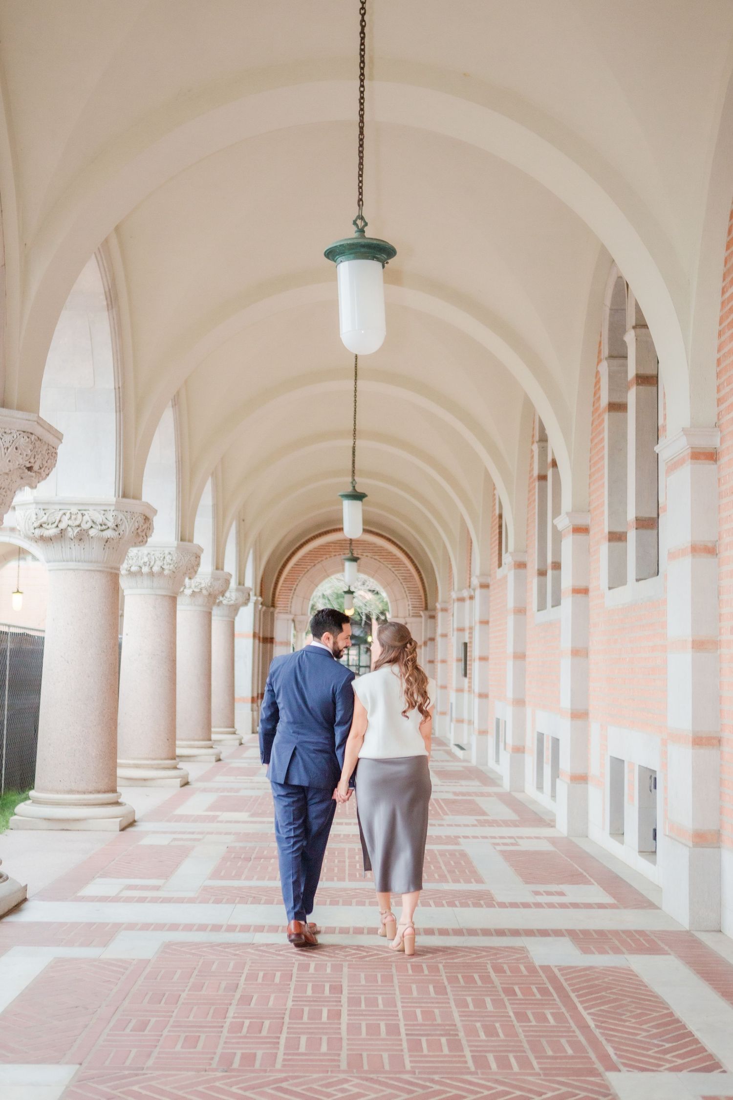 Walking away shot of couple in elegant colonnade with arched ceilings.