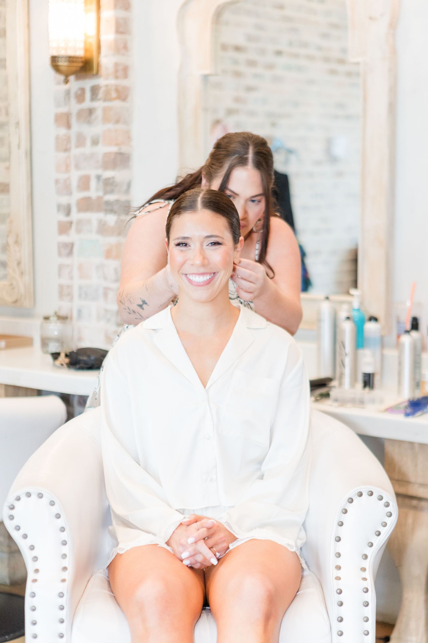 A person in a white robe sits in an elegant white chair during wedding day preparations.