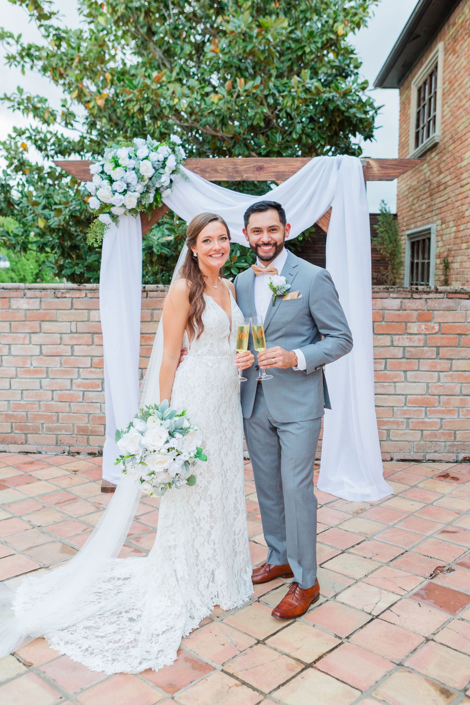 Wedding couple poses for outdoor portraits on a brick patio with white drapery backdrop.
