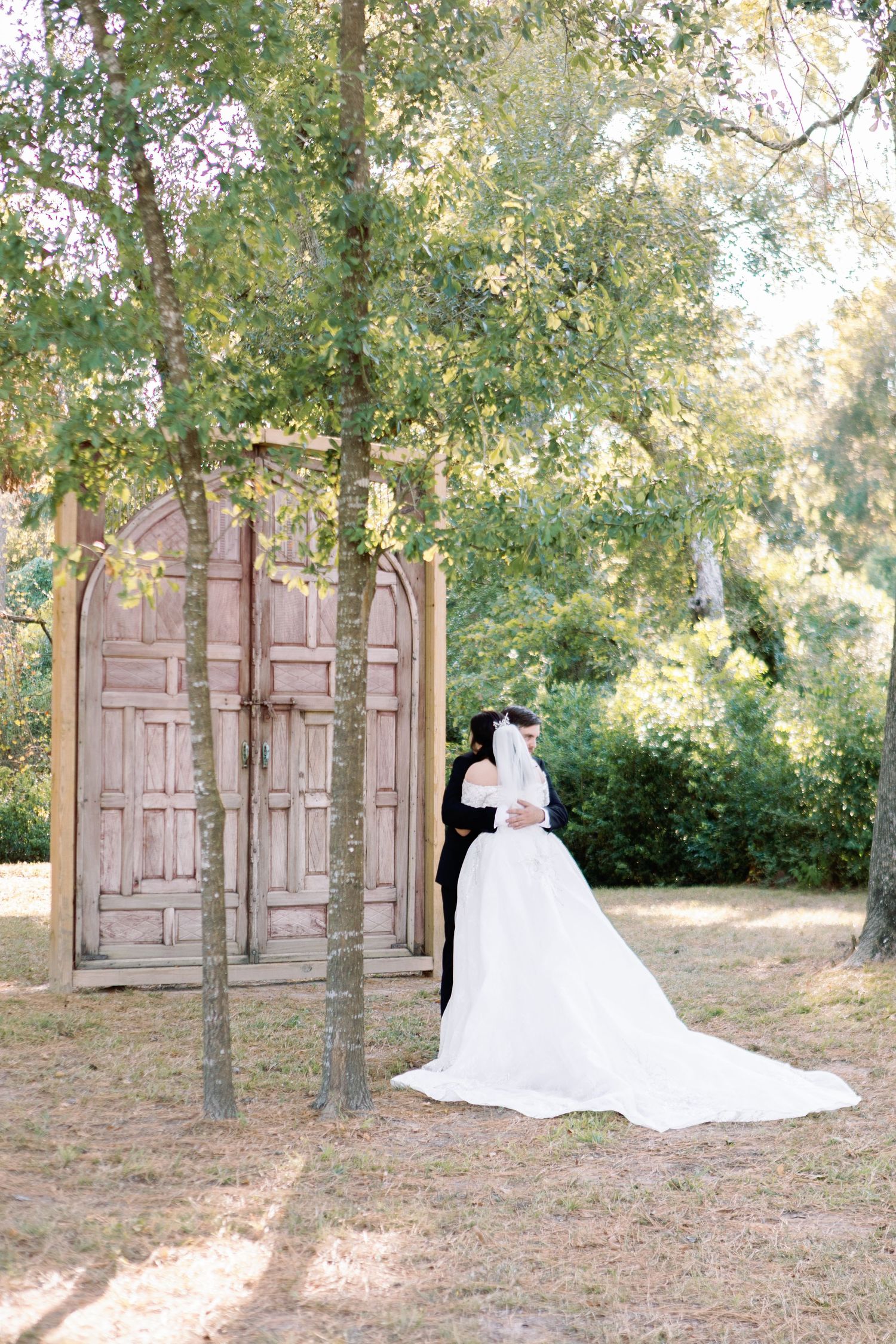 Romantic wedding photo shoot in front of vintage doors under trees in an outdoor garden setting.