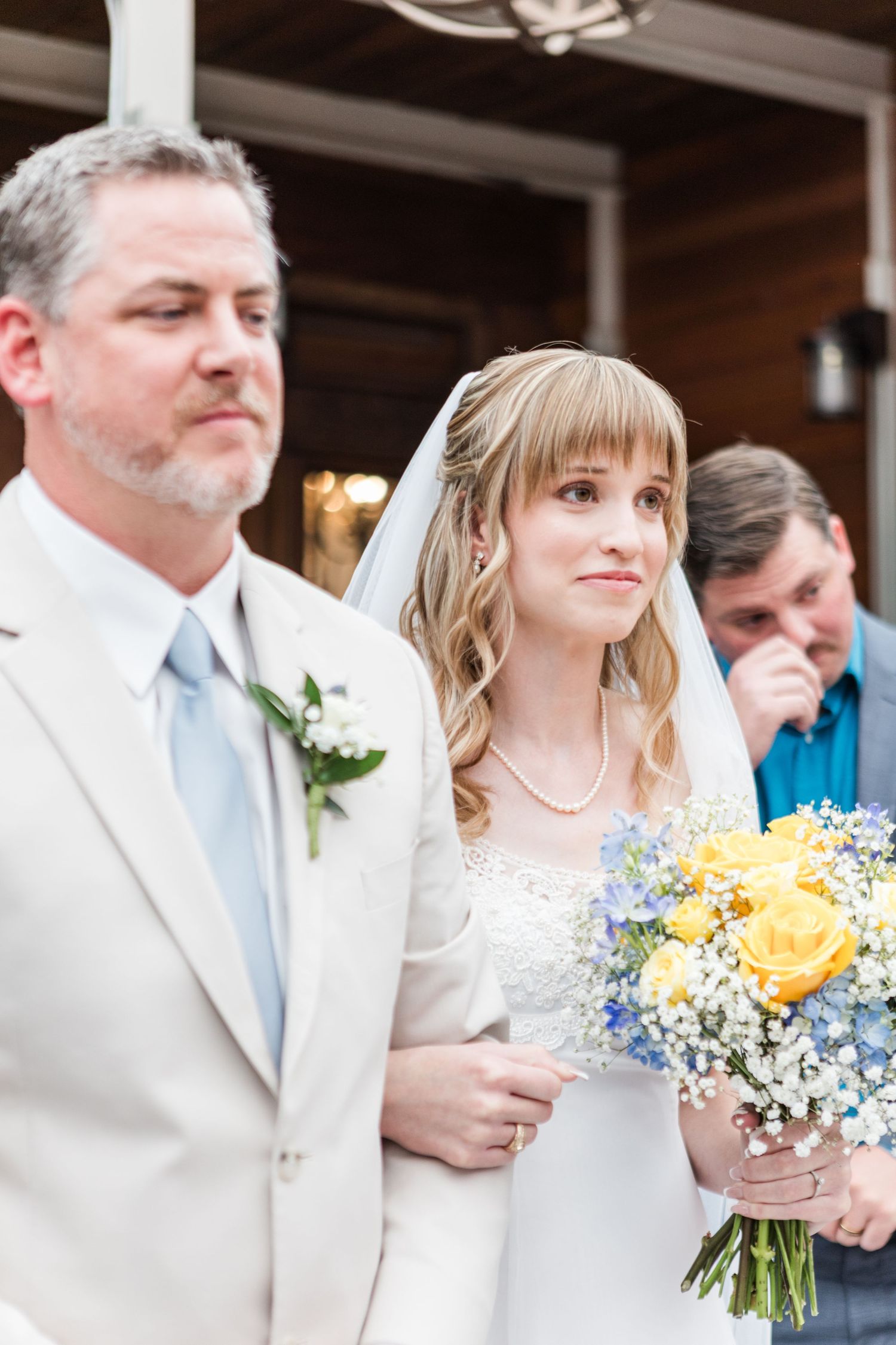 A couple during their wedding ceremony holding yellow and blue flower bouquets.