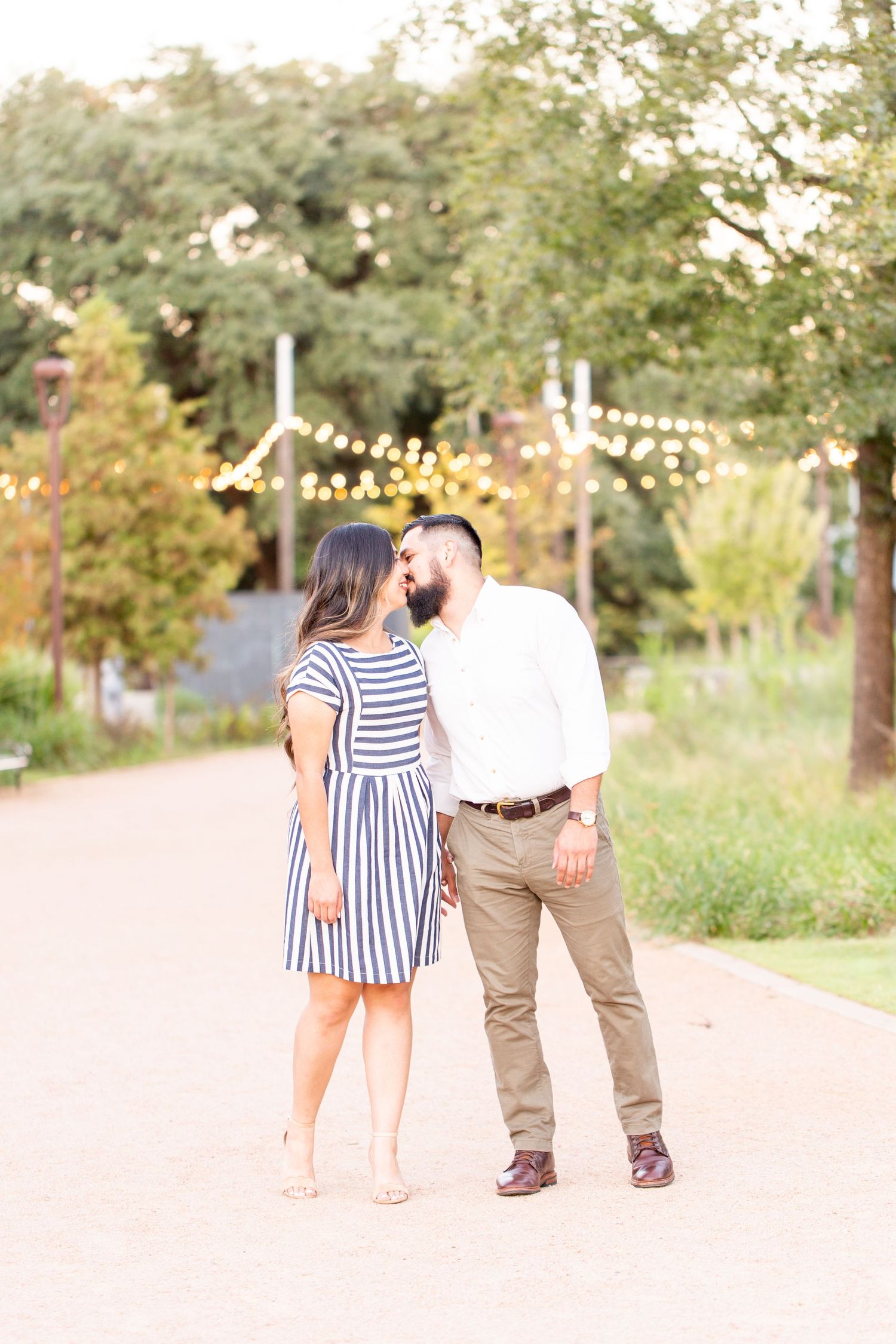 A couple takes romantic engagement photos on a path surrounded by lush summer foliage.