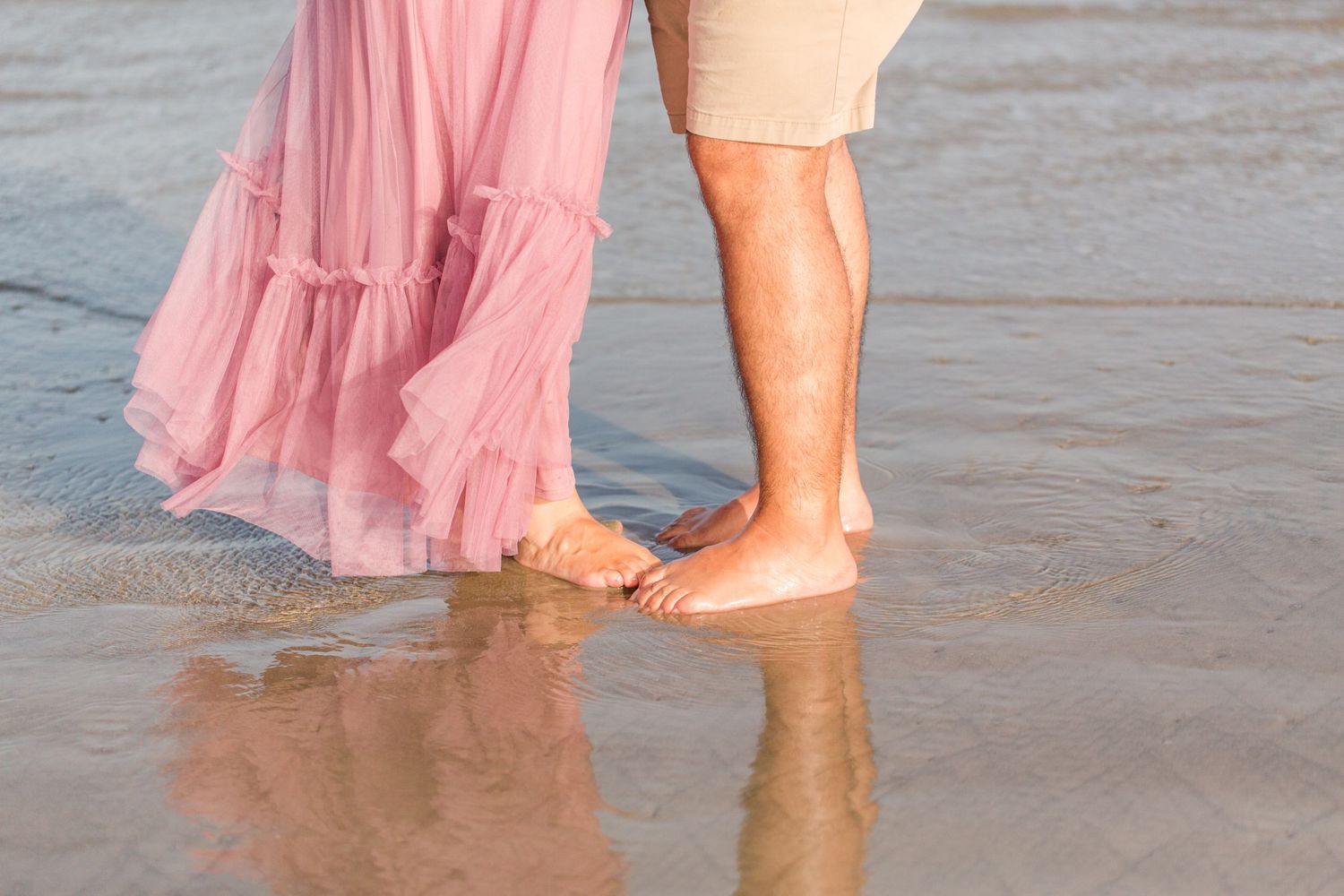 Couple splashing in shallow ocean water wearing pink and white outfits.