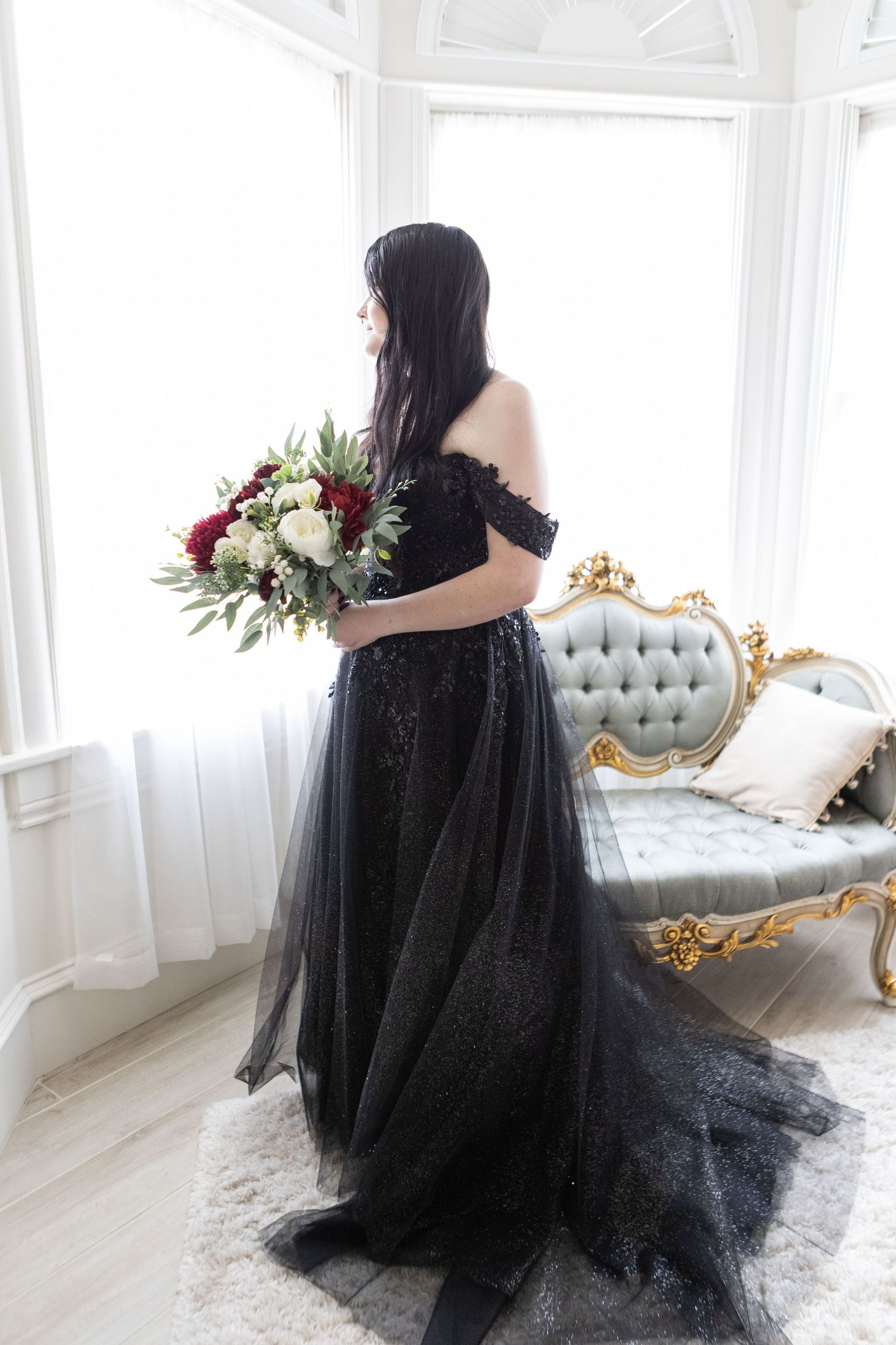 A flowing black tulle gown with off-shoulder detail in a bright white room with elegant furniture.