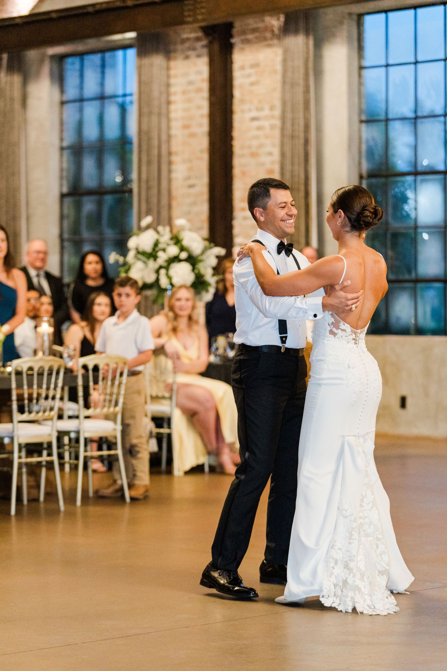Wedding couples dancing together in an industrial-style venue with exposed brick walls and tall windows.