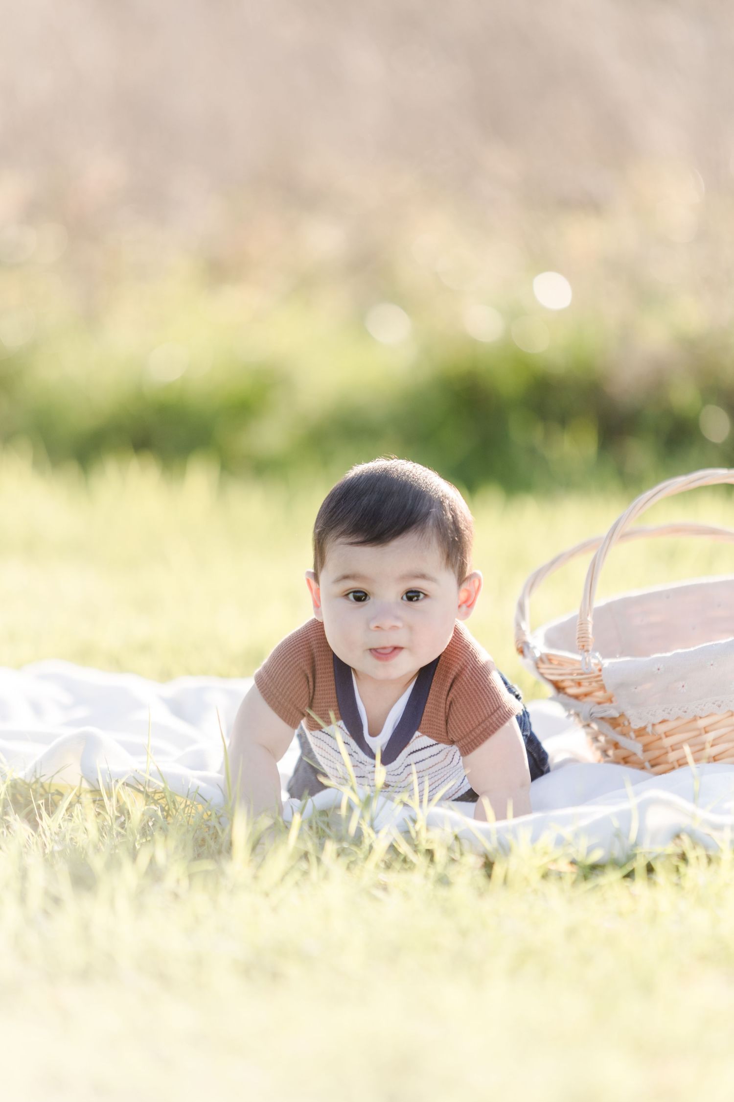 Baby lying on stomach on white blanket during outdoor photo shoot.