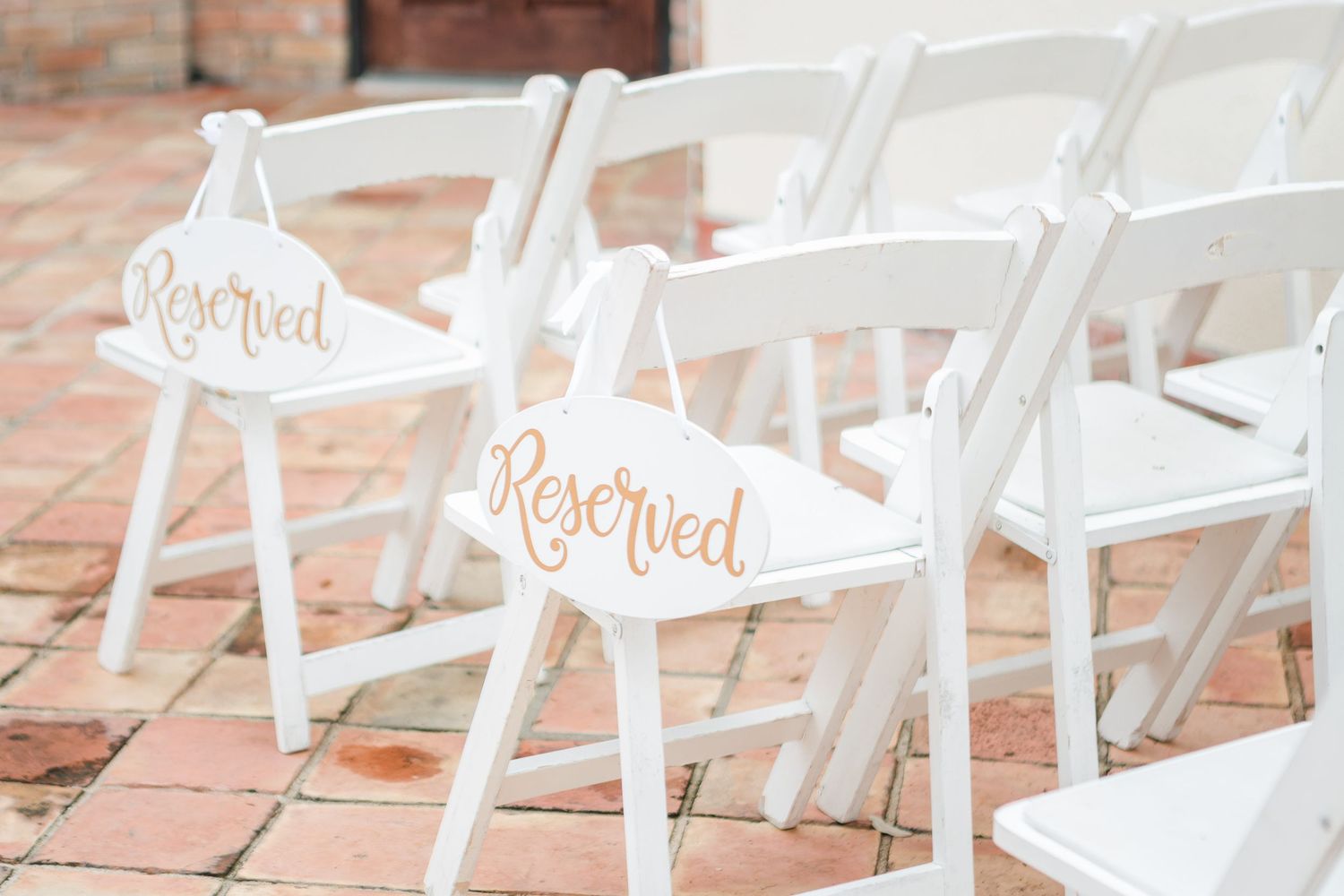 White folding chairs arranged in rows on a brick patio for an outdoor wedding ceremony.