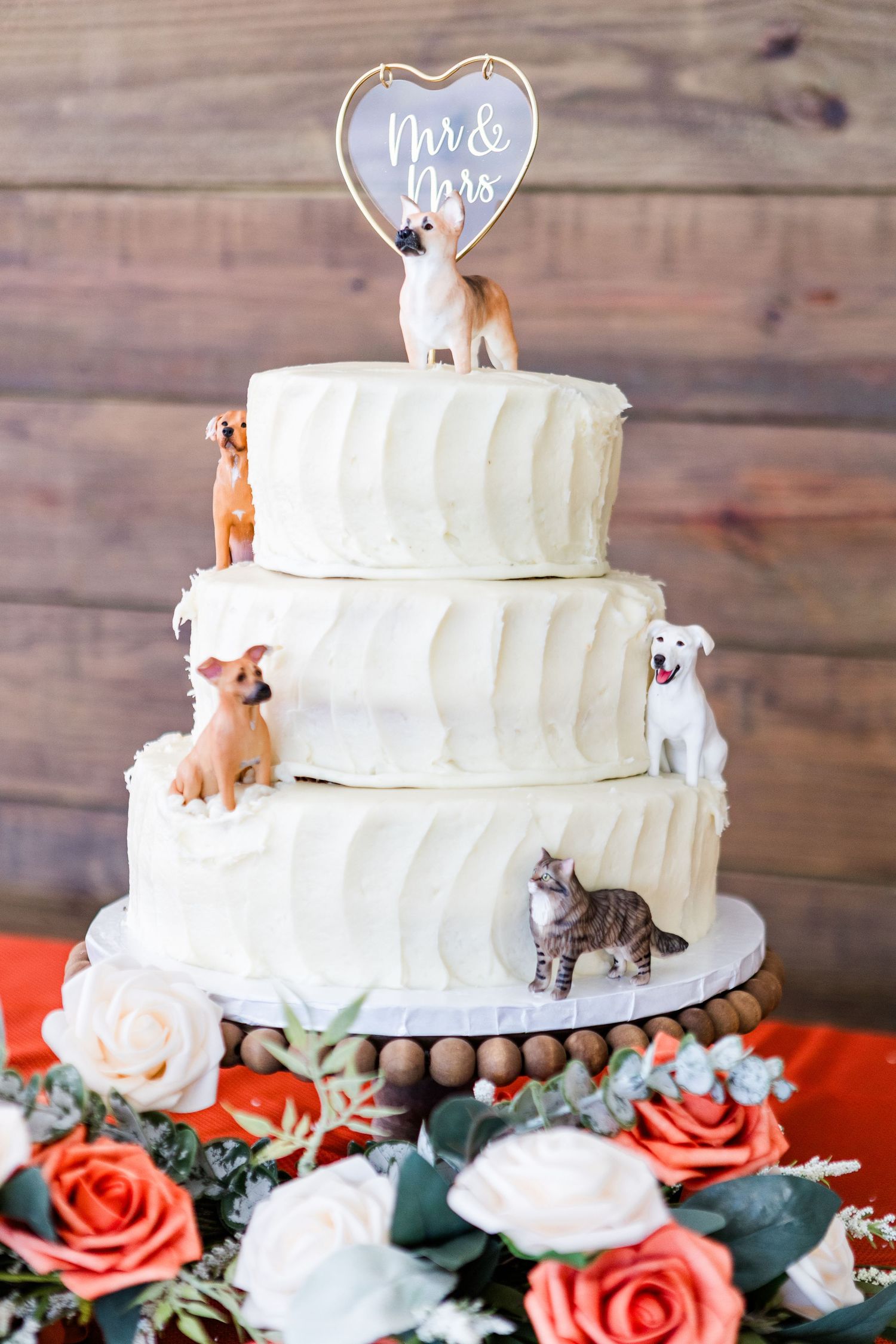 White tiered wedding cake with pet figurines and Mr & Mrs topper surrounded by coral flowers.
