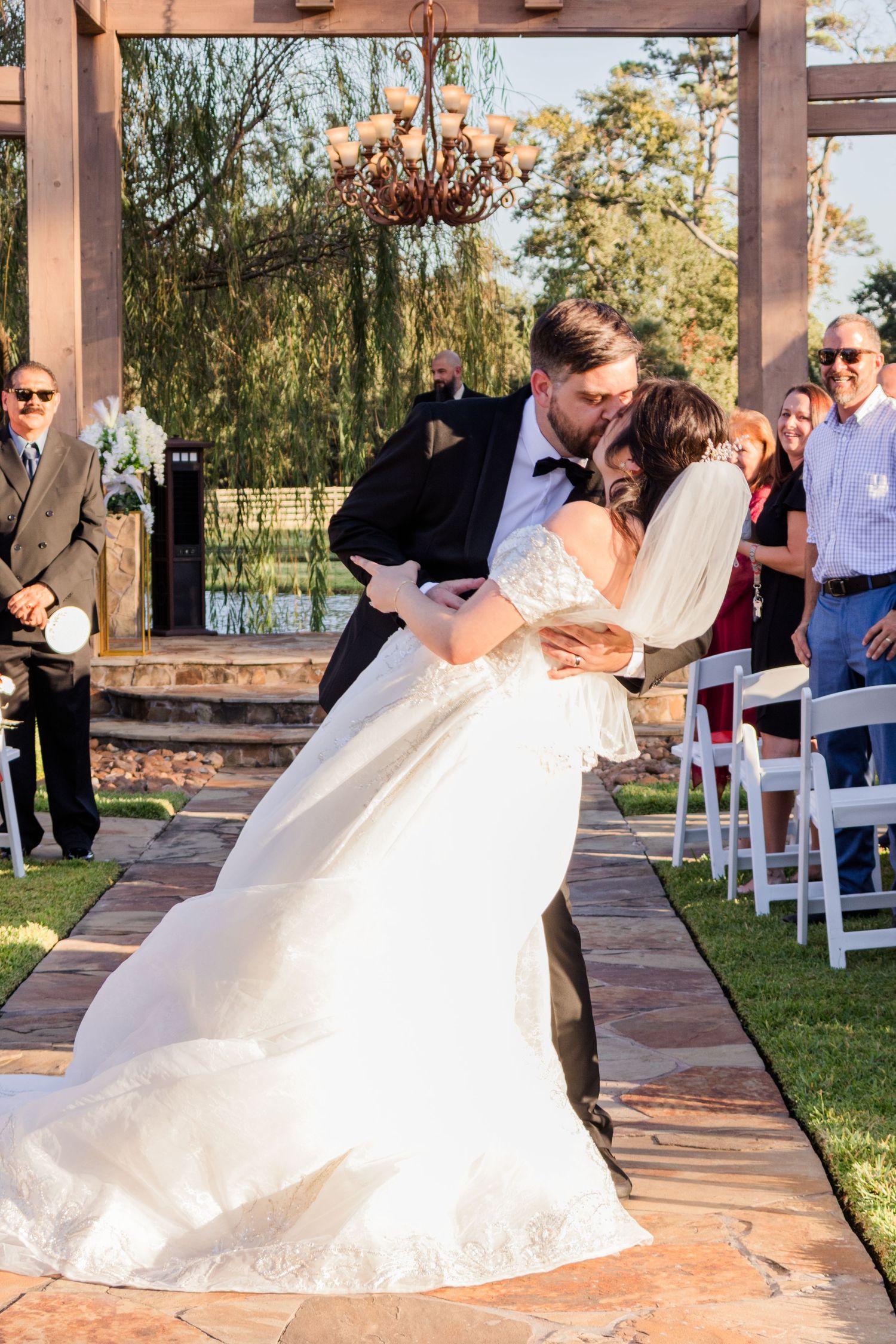 Wedding ceremony celebration with guests seated outdoors under a wooden pergola.