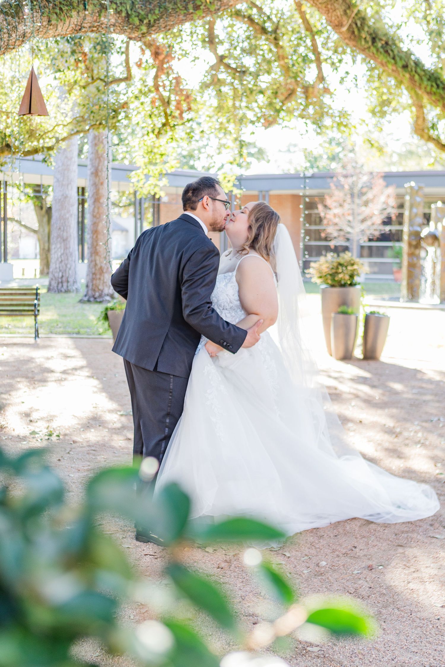 Wedding couple shares romantic moments in an outdoor garden setting with natural light filtering through trees.