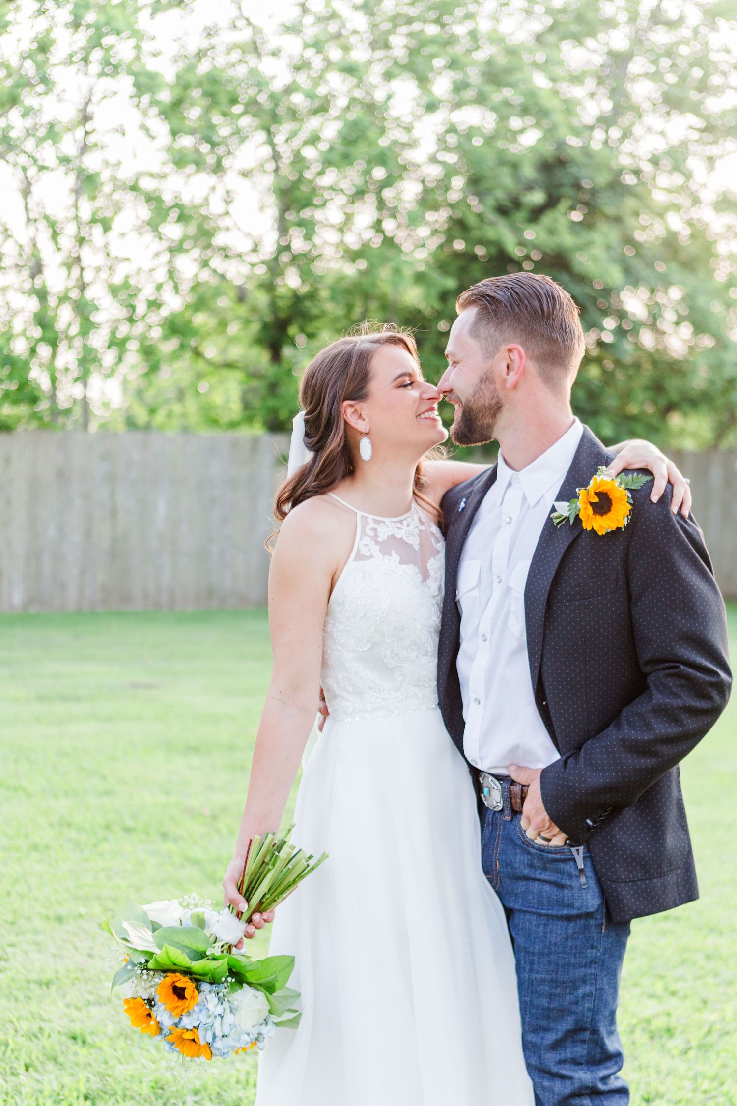 Wedding couple sharing romantic moments in a garden setting with sunflower bouquet.