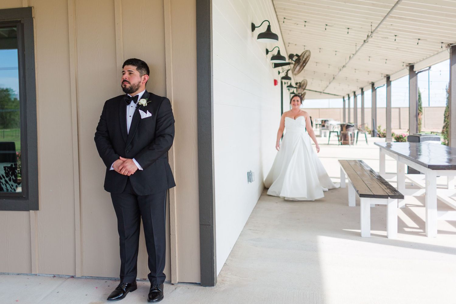 First look wedding moment captured at outdoor venue with couple separated by wall.