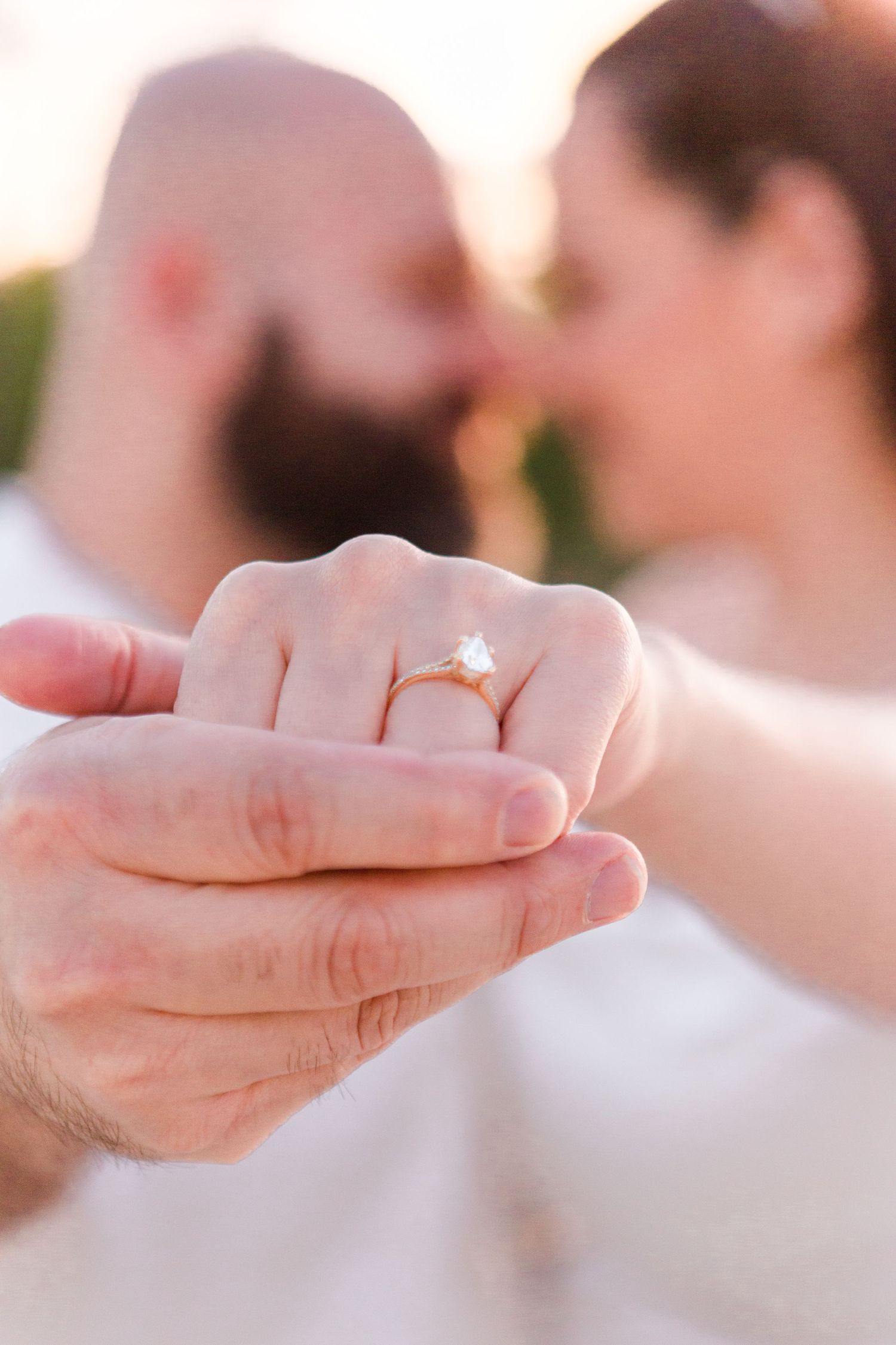 Close-up of hands showing engagement ring in soft natural lighting.