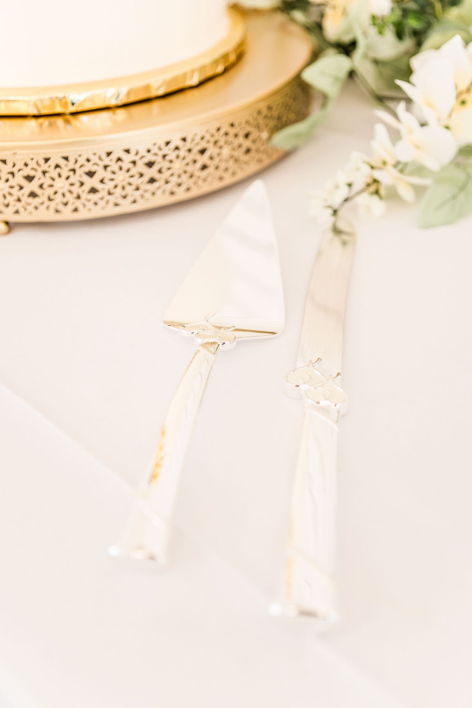 Gold detailed cake stand with white floral decorations and greenery.