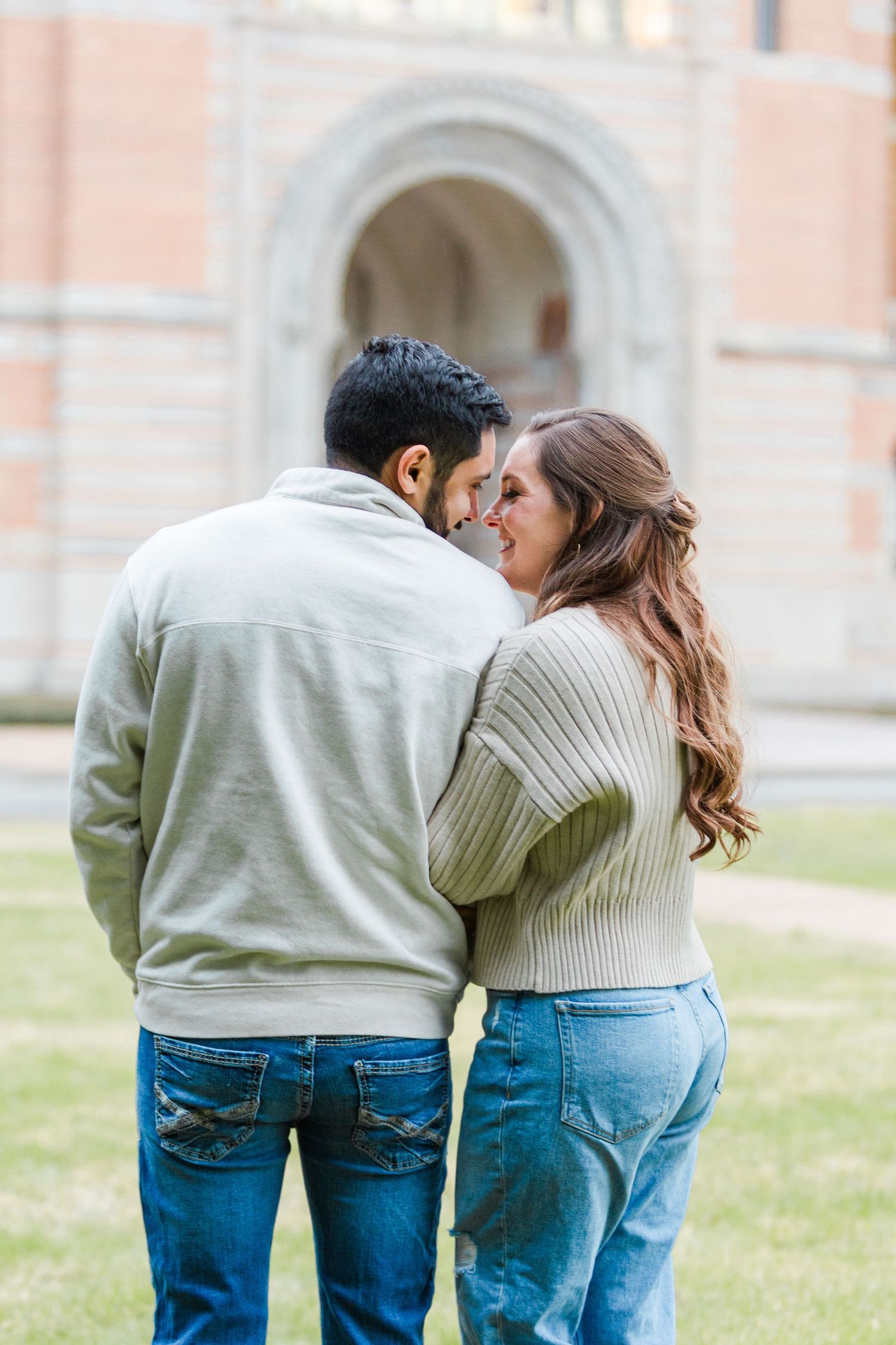 Romantic couple in casual outfits sharing an intimate kiss against a brick building backdrop.