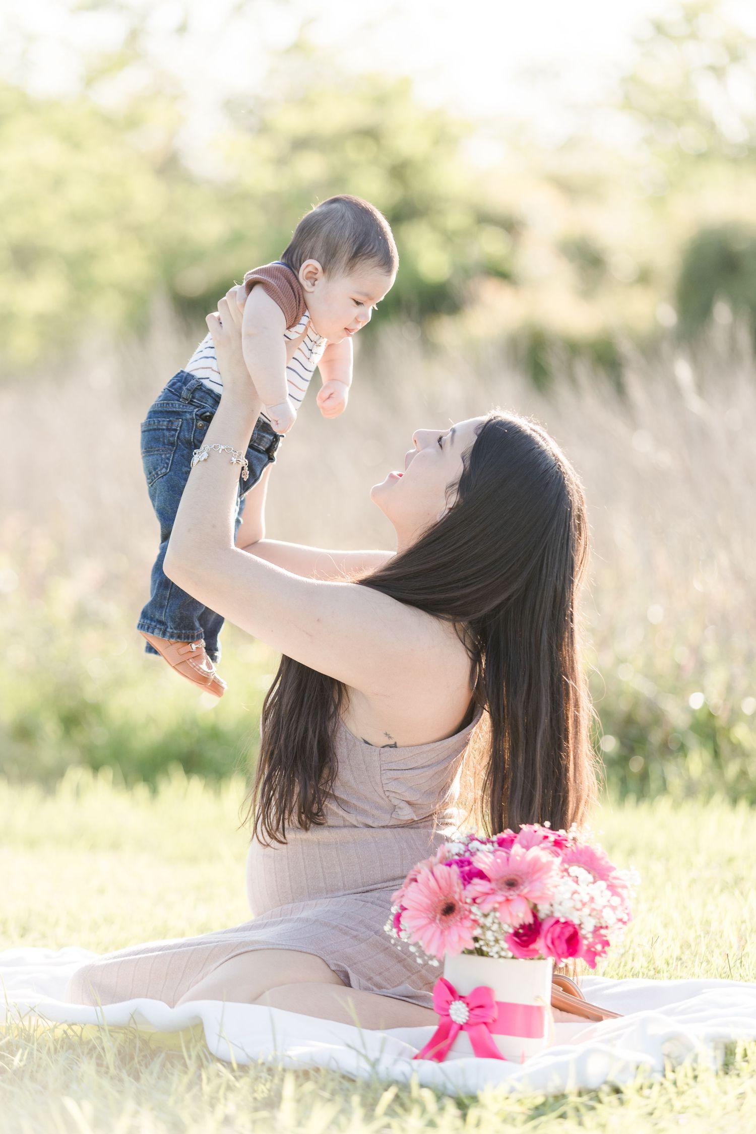 Mother and child sharing tender moments on a blanket outdoors with pink flowers.