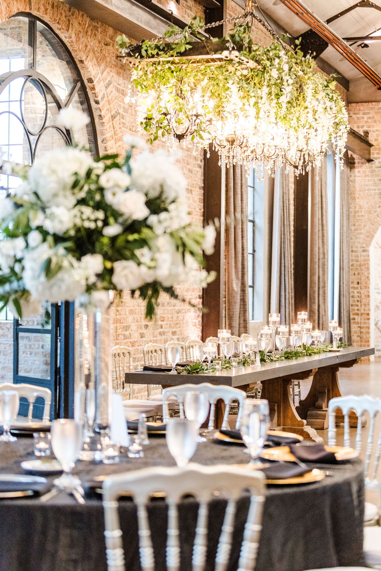 Luxurious wedding reception decor with chandeliers, white florals and brick wall details.