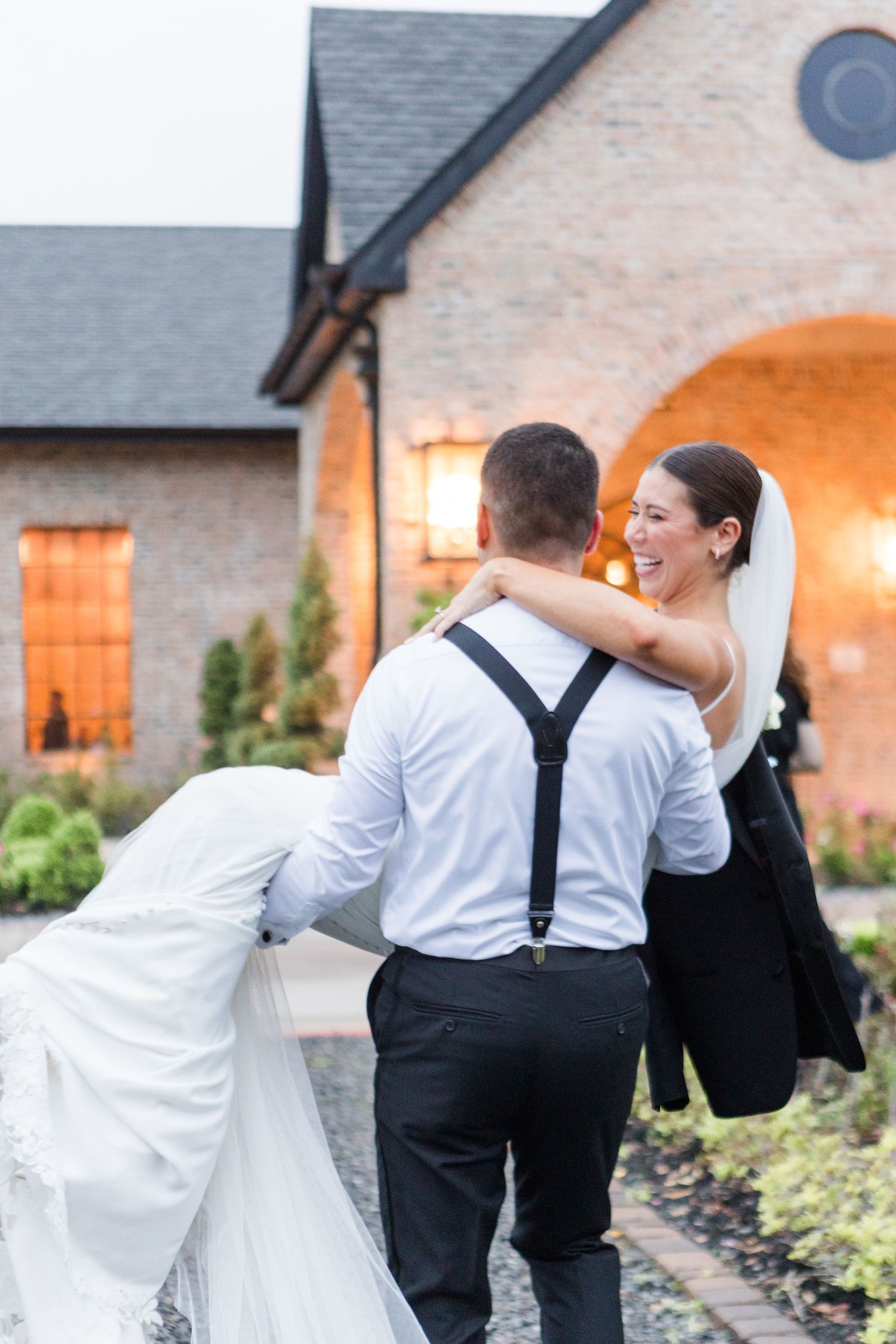 A joyful couple shares candid moments while walking on a path outside their wedding venue at sunset.