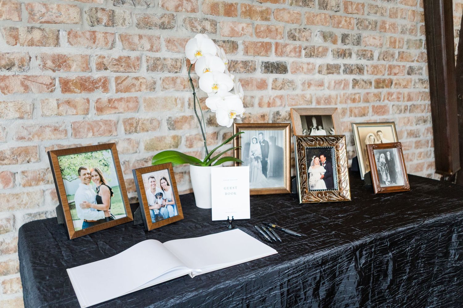 Memory table with framed photos displayed on black tablecloth at wedding reception.