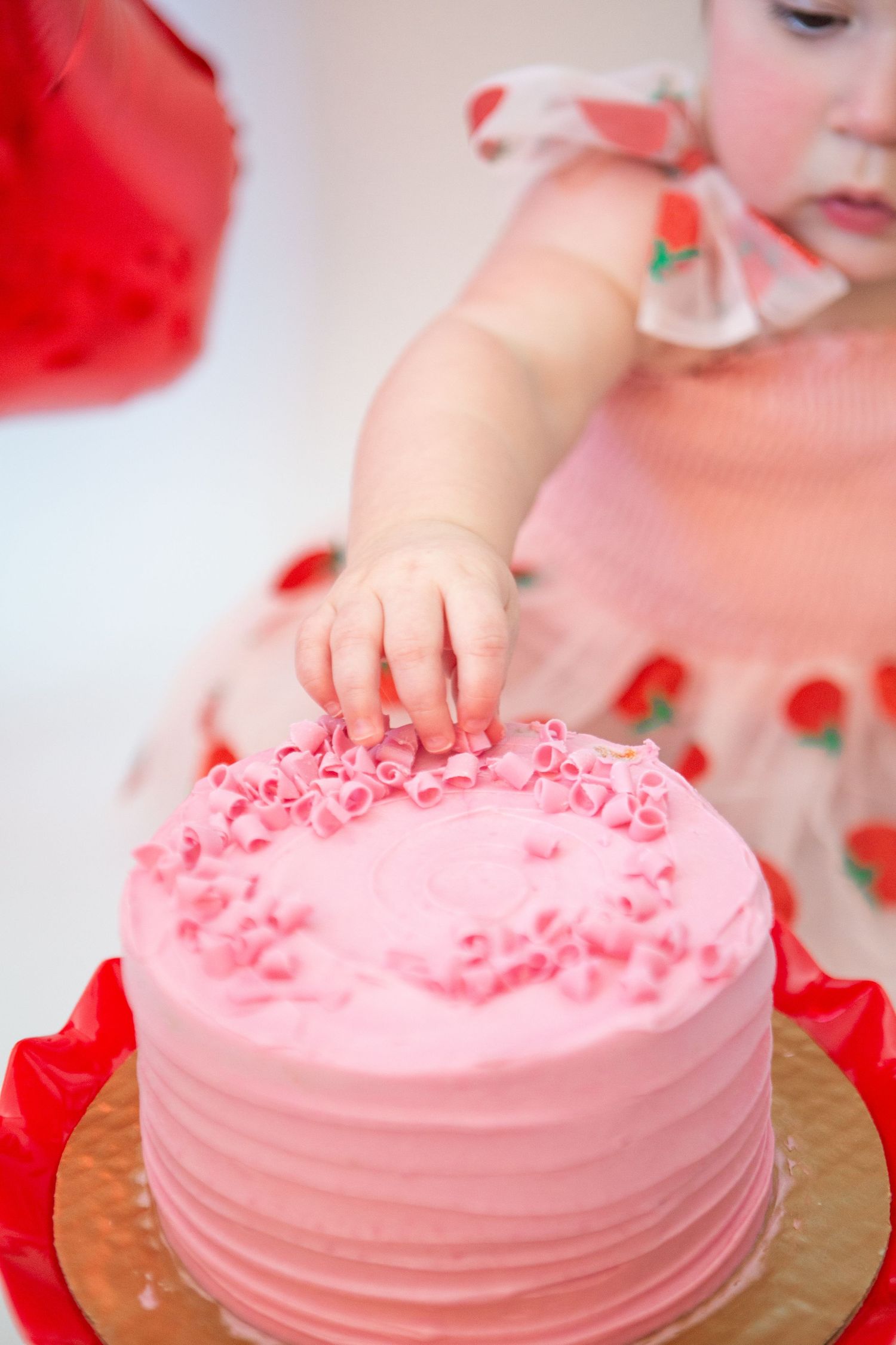 Pink frosted celebration cake with sprinkles against white background.
