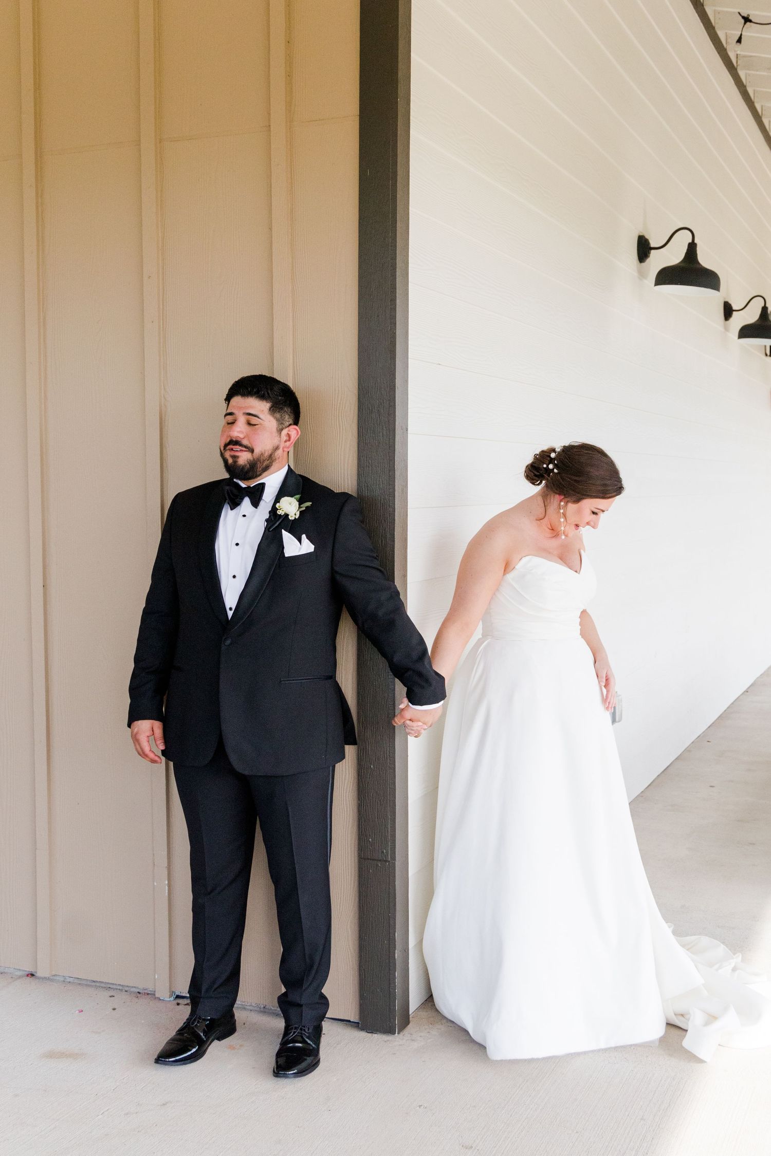 A wedding couple poses playfully around a corner in black and white formal attire.