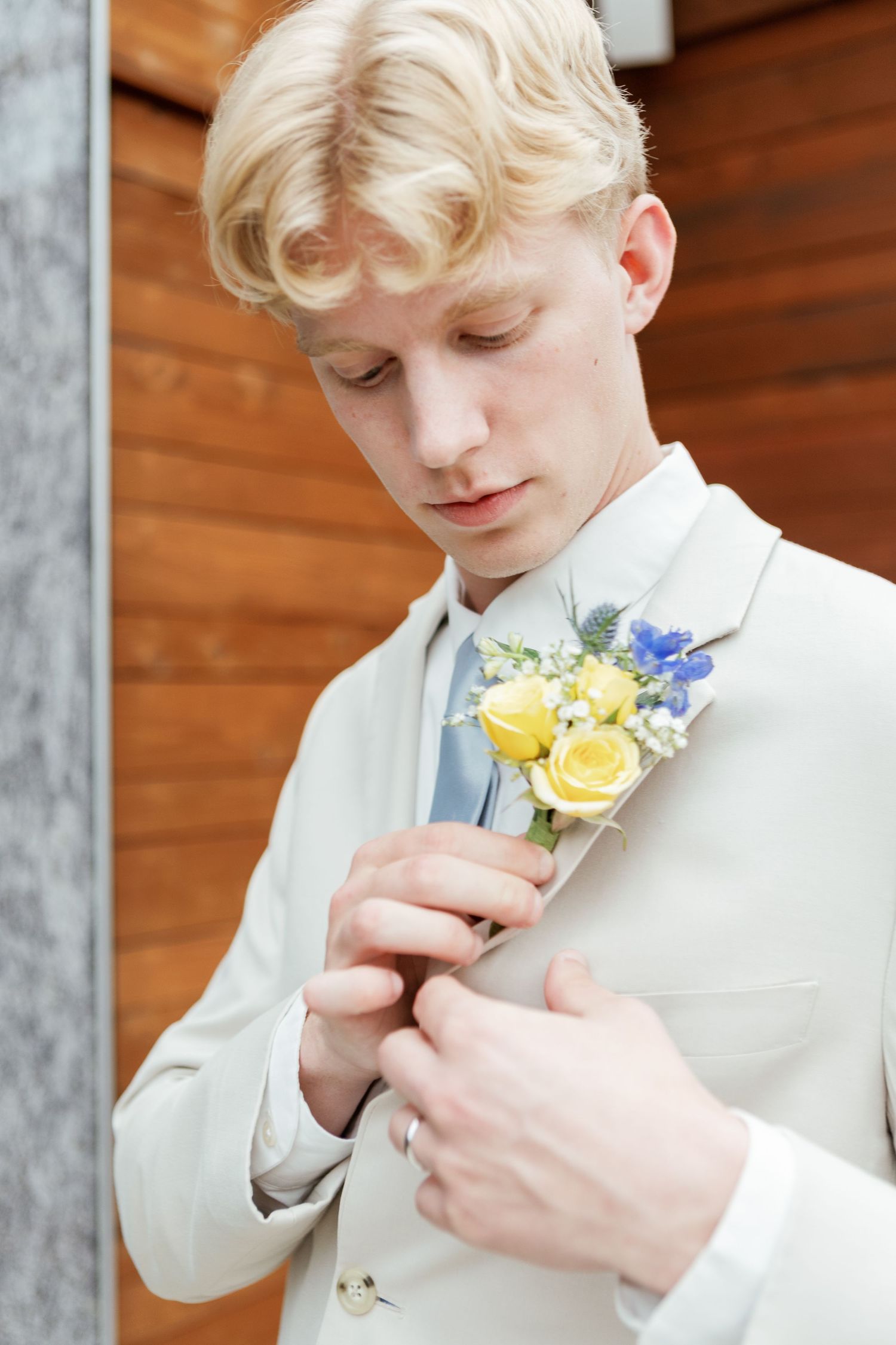 Person in white suit adjusts yellow and blue floral boutonniere.
