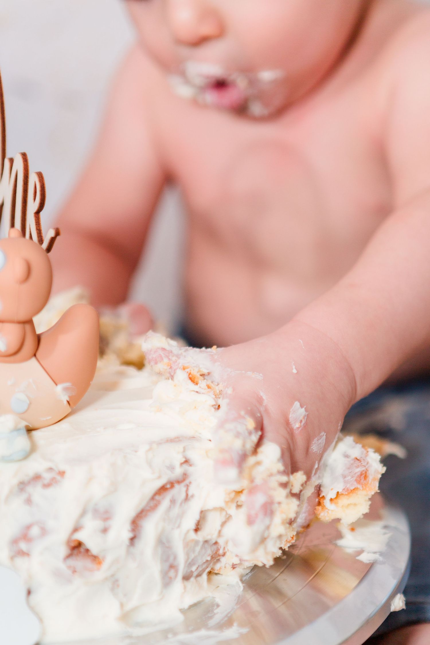 Close-up of tiny hands playing with white birthday cake frosting.