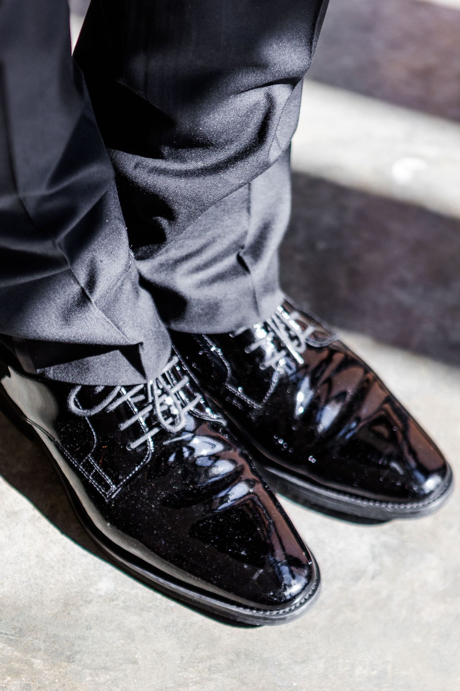 Close-up of shiny black formal dress shoes on concrete floor.
